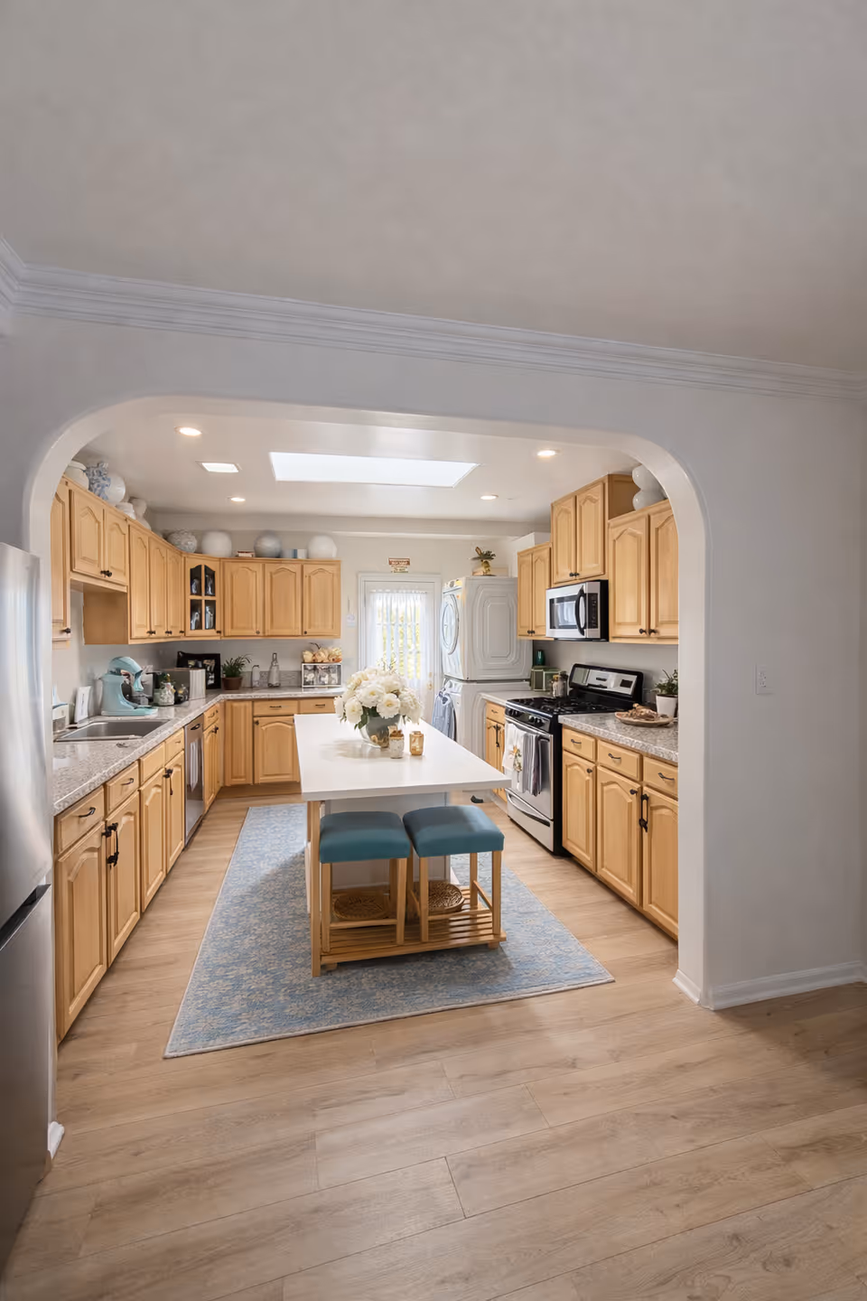 Bright kitchen with wooden cabinets, island, and teal stools in a senior living facility.