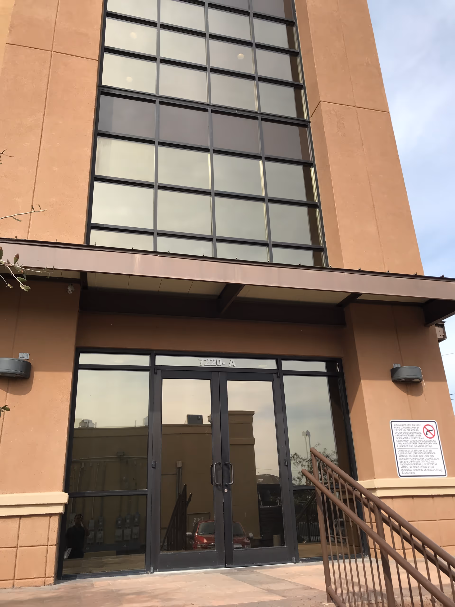 Tall tan building with large glass entrance doors and a metal railing at front.