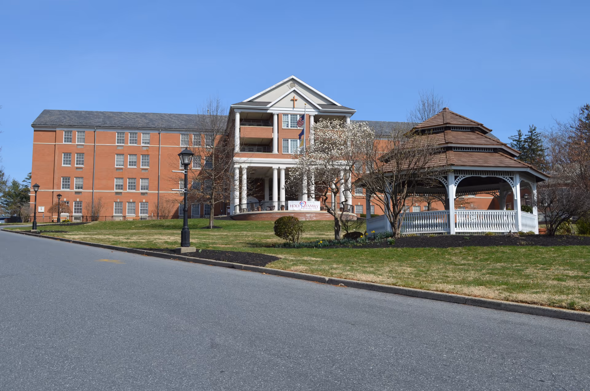 Front view of Holy Family Senior Living campus featuring brick building and a white gazebo.