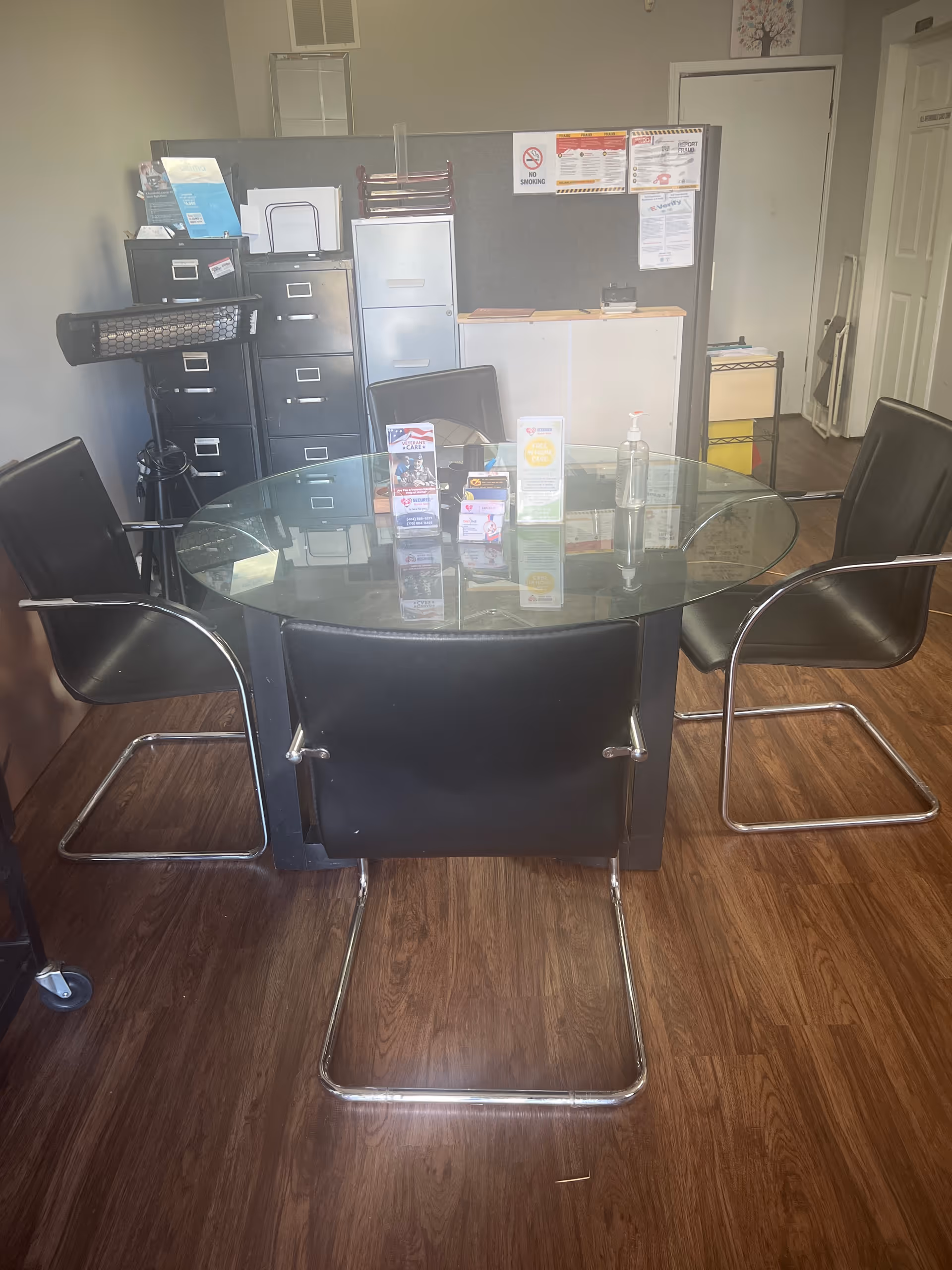 A glass round table with four black chairs sits in a small reception area.