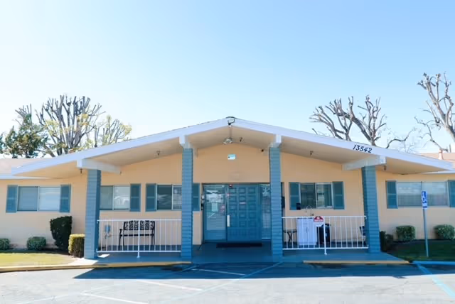 Front view of a single story pastel facility for seniors with blue pillars.