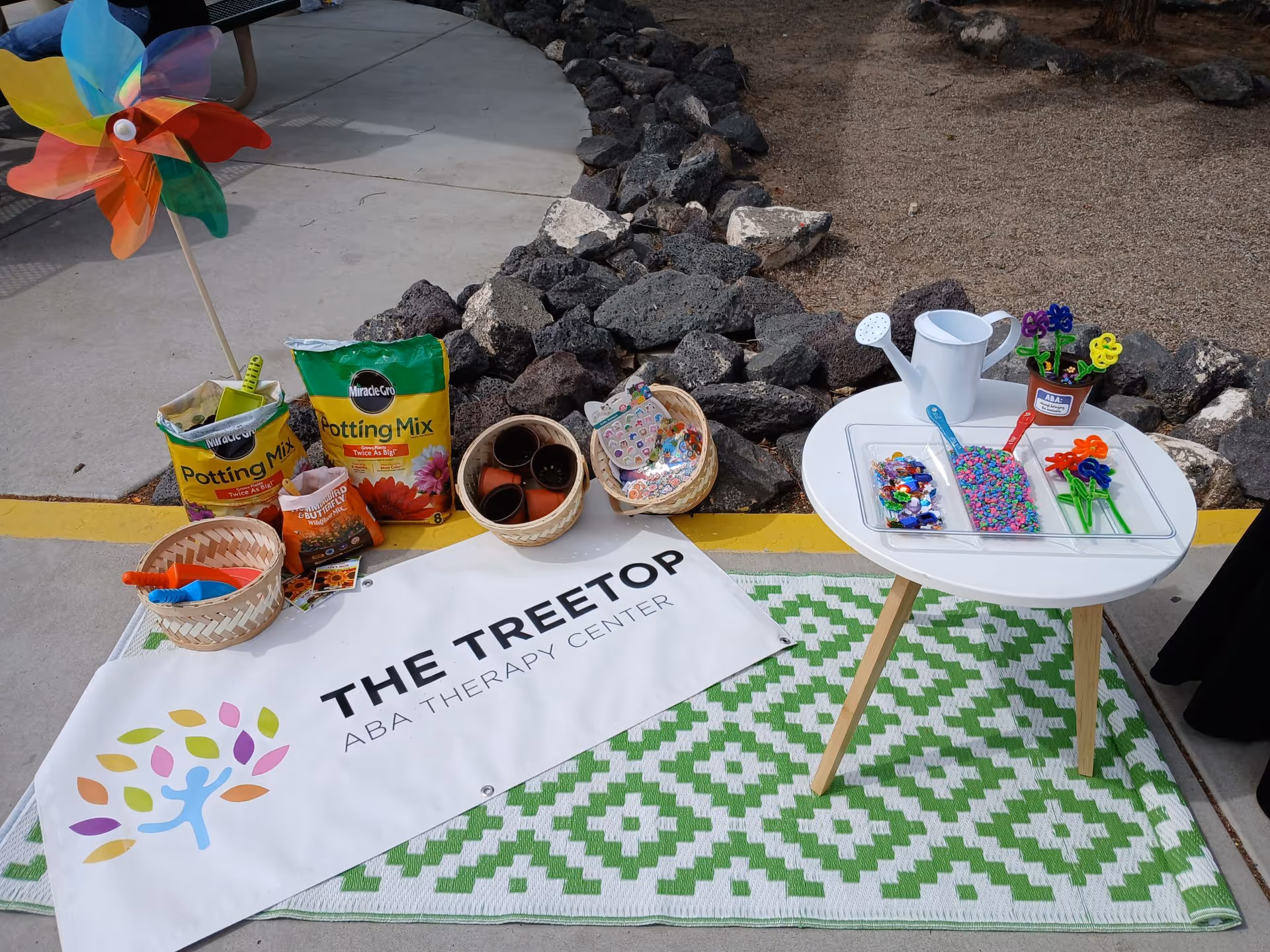 Outdoor therapy setup with tables, gardening supplies, and a banner for The Treetop ABA Therapy.
