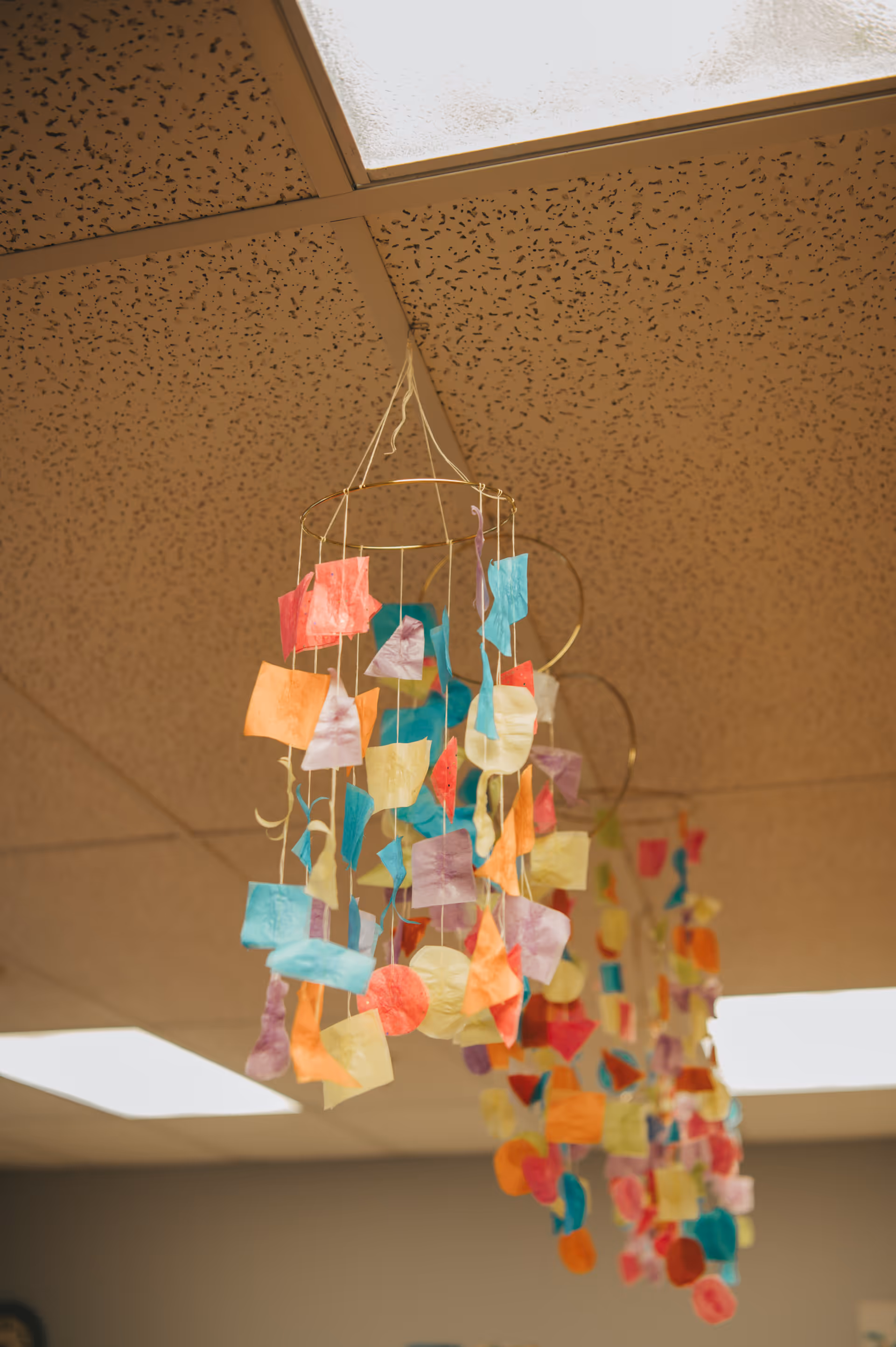 Colorful tissue decorations hang from a dropped ceiling in a senior living facility lobby.
