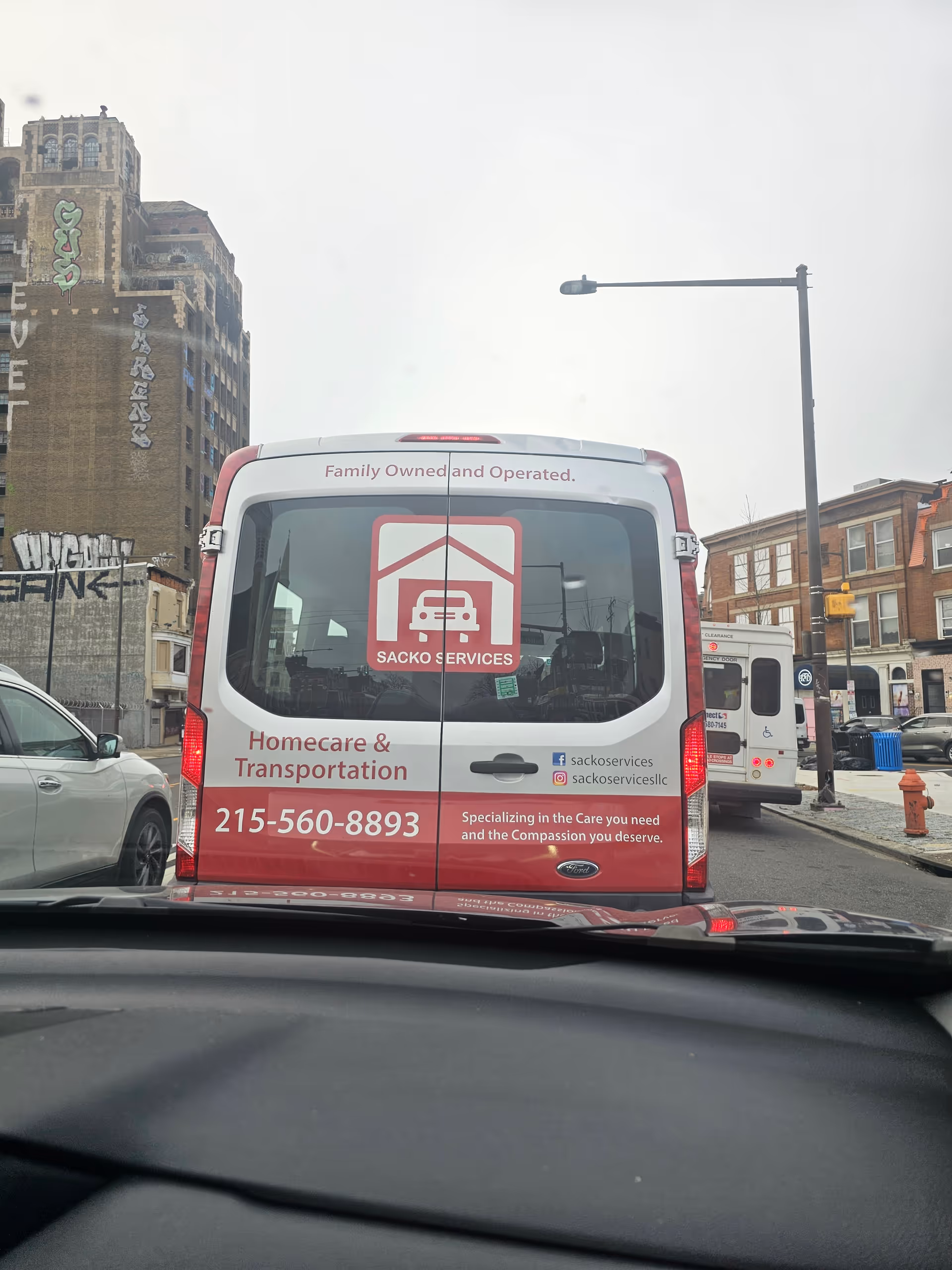 Rear view of Sacko Services van on a city street, showing homecare transportation signage.