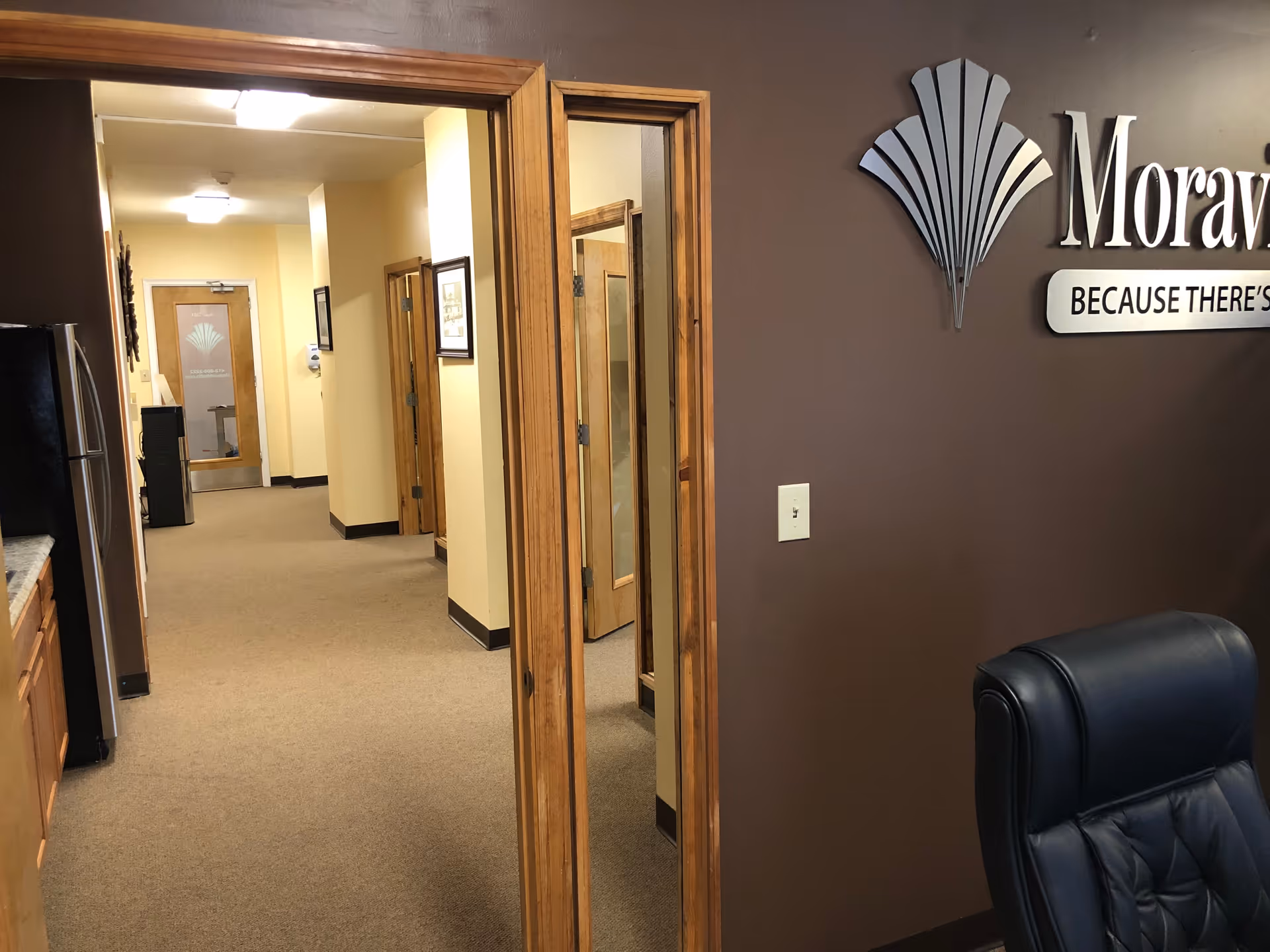 Interior hallway at Moravia Health Pittsburgh with doors, brown walls, and a leather chair.