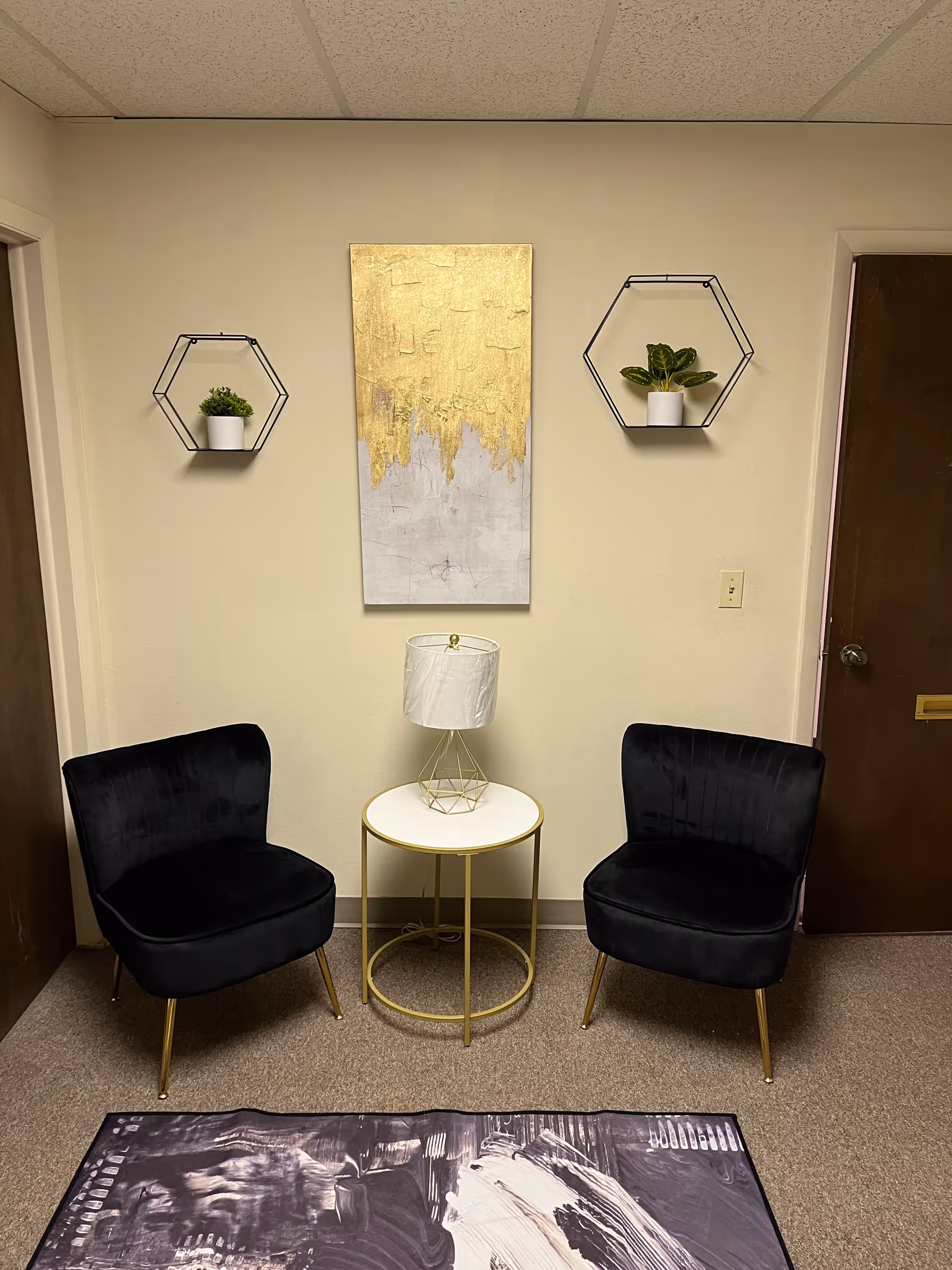 Two black cushioned chairs flank a white round table with a lamp in a small hallway.