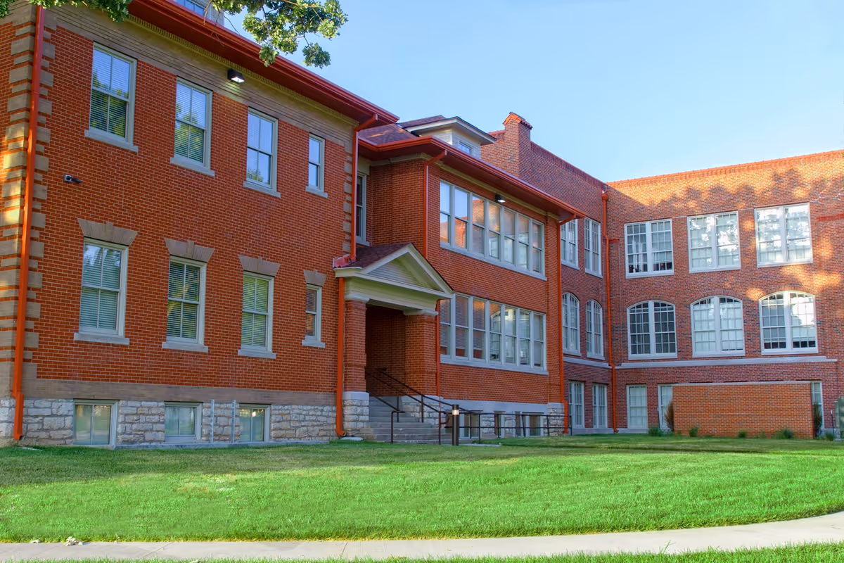 Red brick senior living facility exterior with large windows and green lawn.