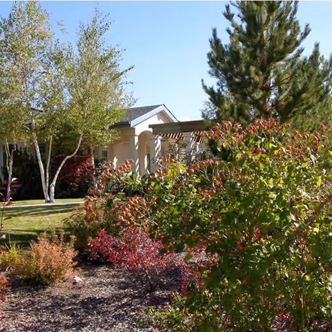 Senior living facility exterior with landscaped garden and trees.