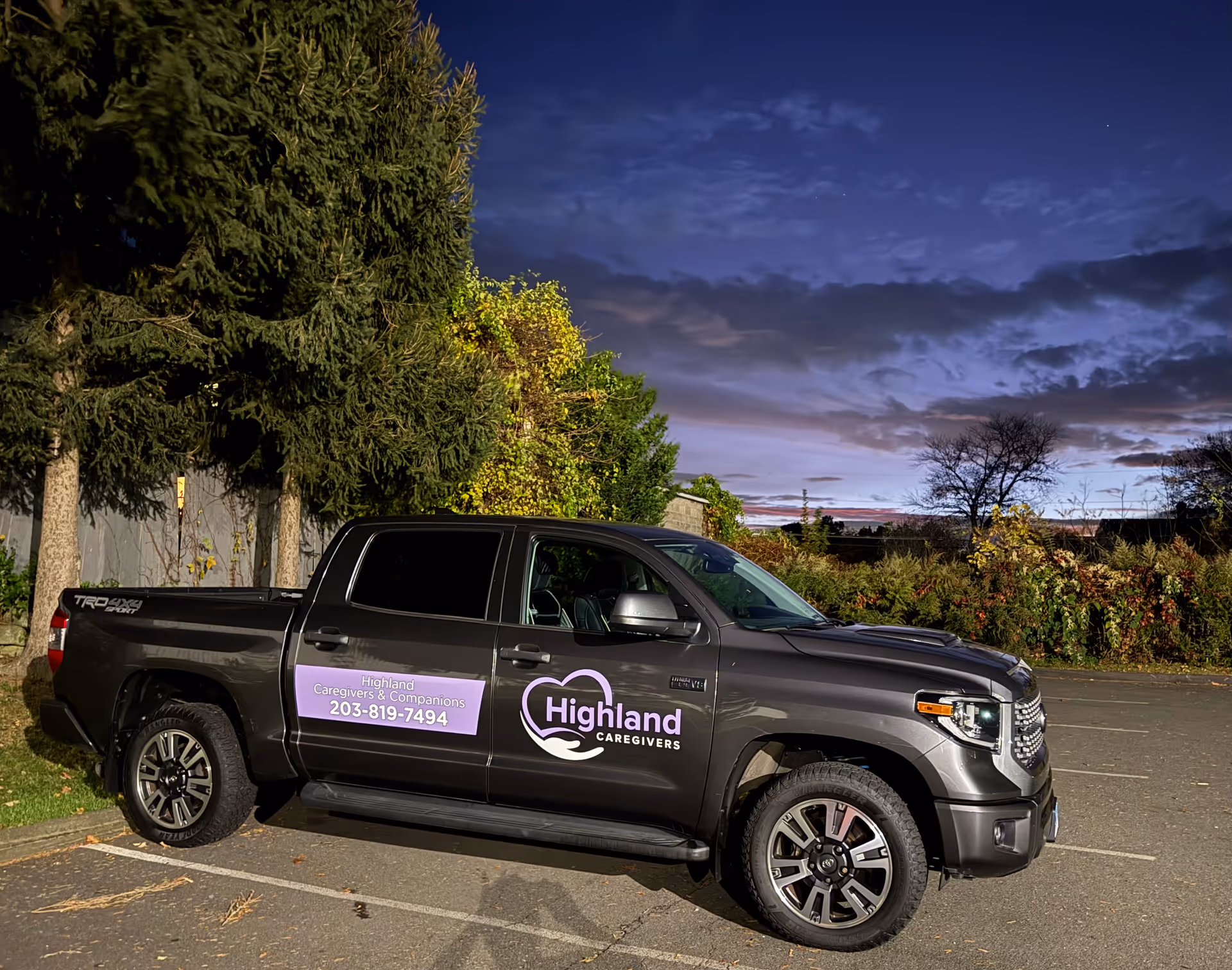 Dark gray Highland Caregivers pickup truck with logo parked in a lot at dusk.
