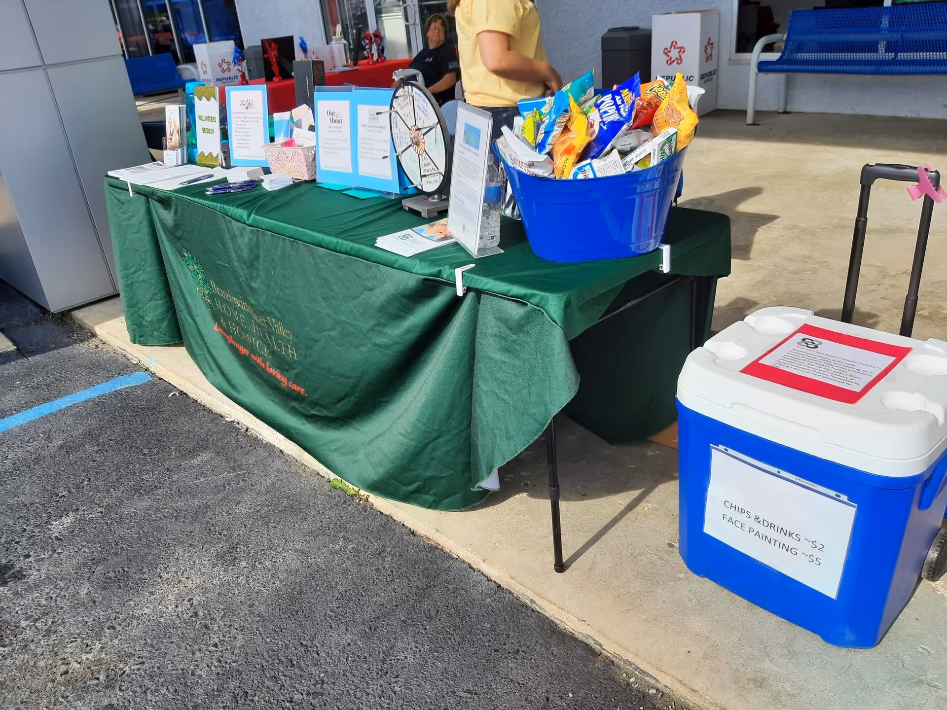 Outdoor table with brochures, snacks, and a blue cooler near the facility entrance.
