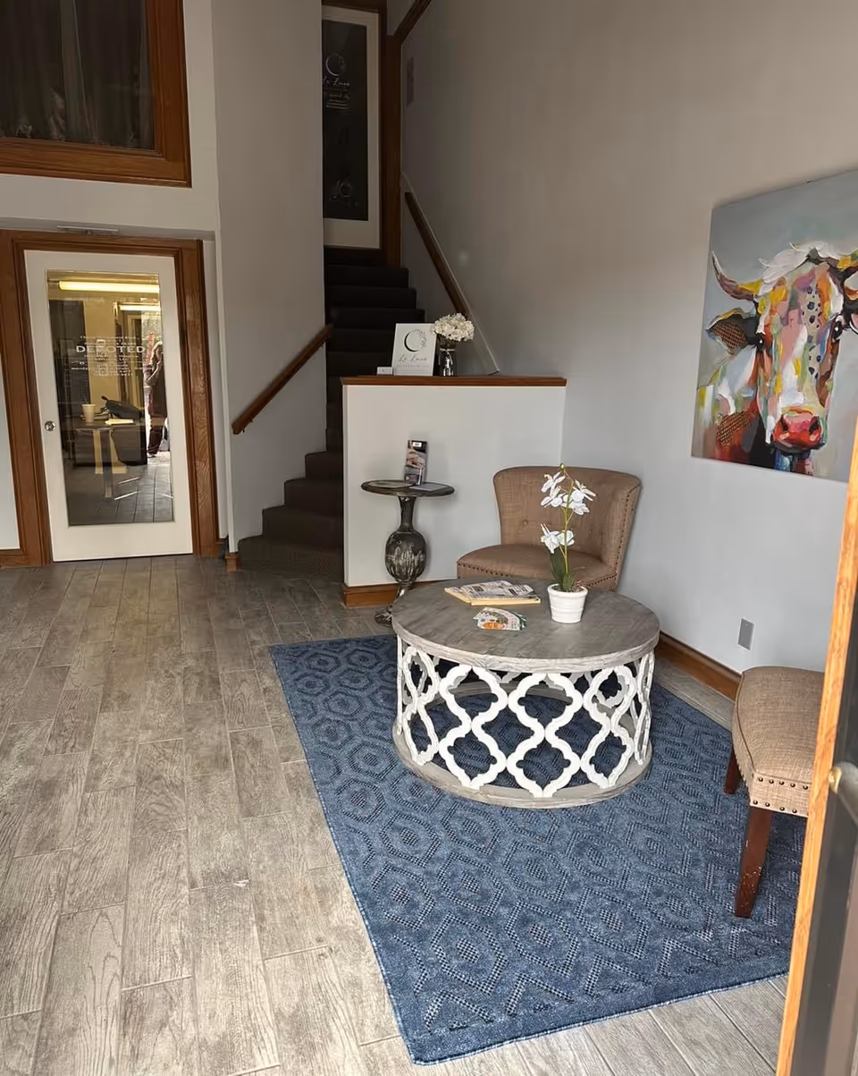 Interior lobby with seating area, round table, two chairs, stairs, and cow artwork.