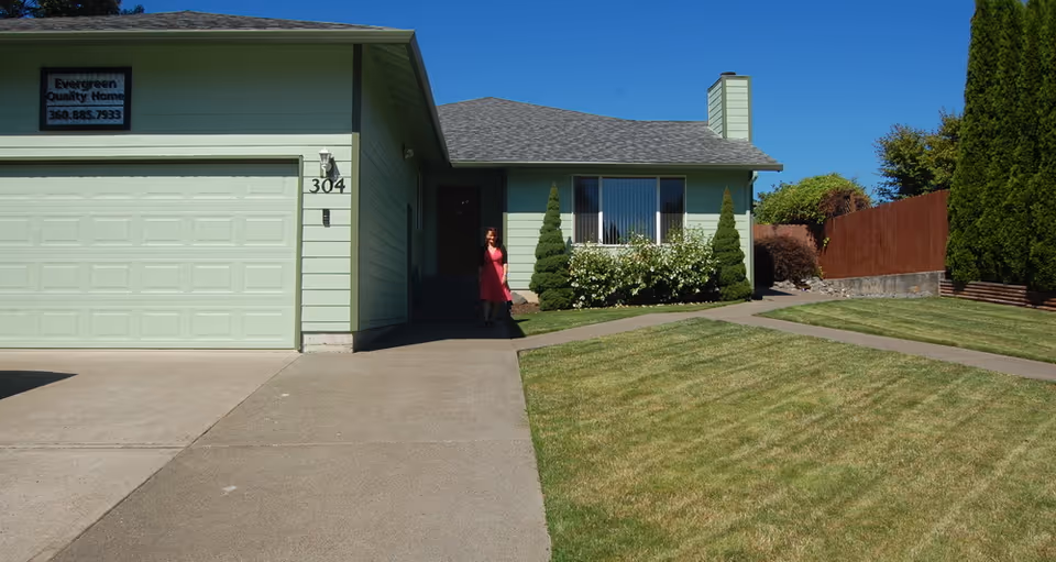 Green, single-story home with driveway, front yard, and a person near the entrance.