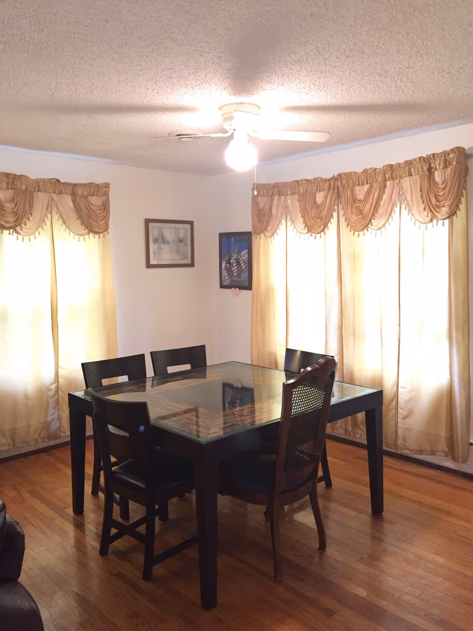 Dining room with a glass-top table, six chairs, beige curtains, and a ceiling fan.
