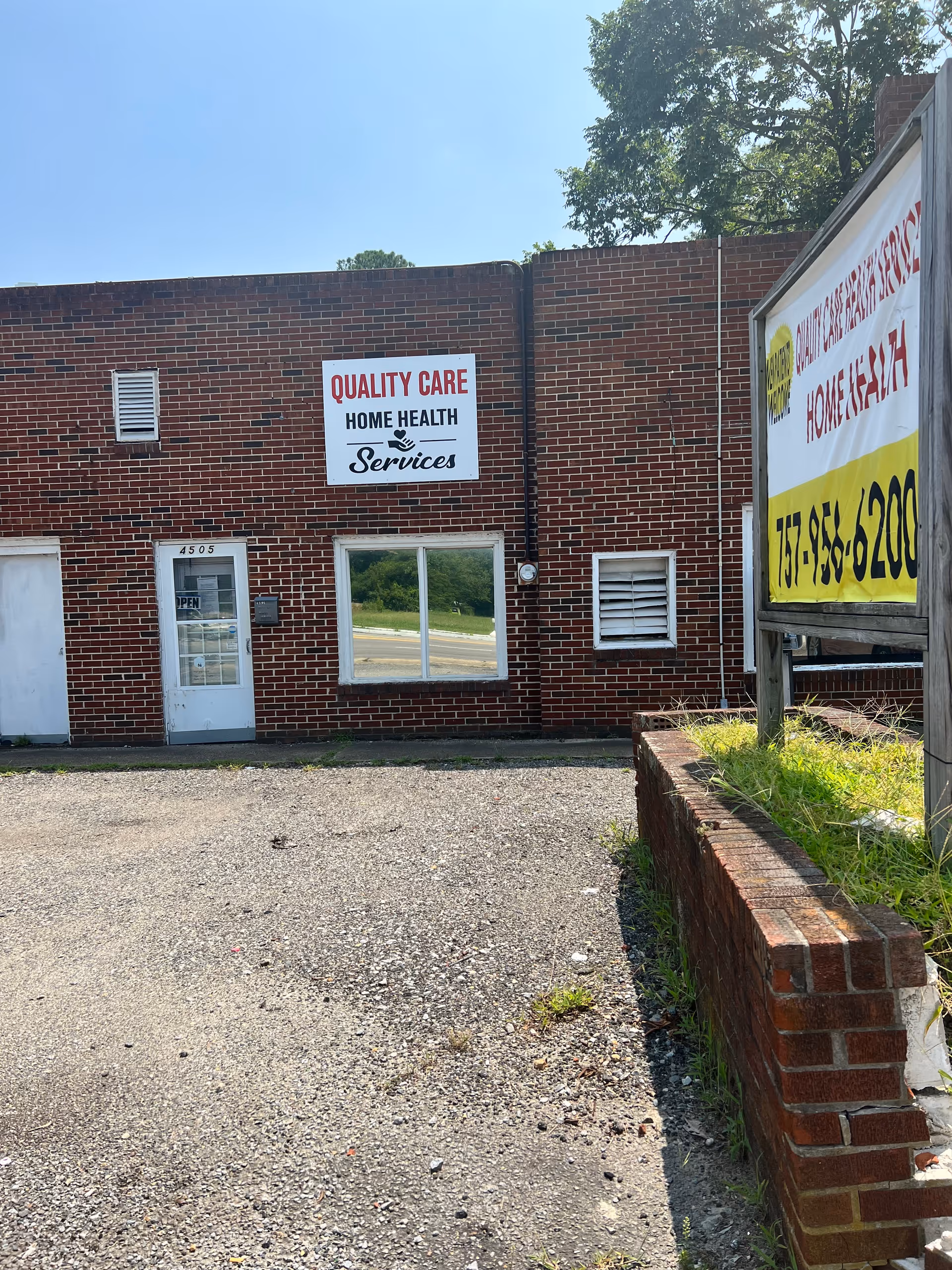 Brick building exterior with Quality Care Home Health Services sign, door, window, and gravel lot.