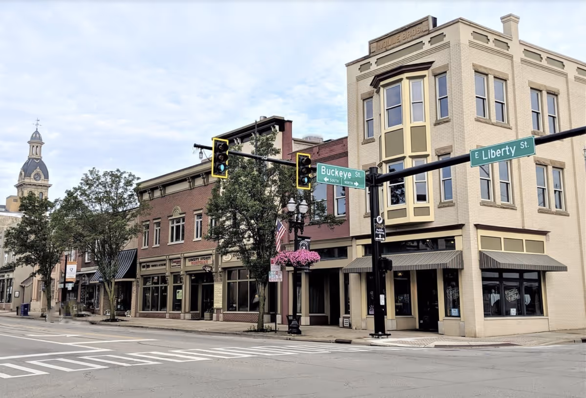 Downtown street corner with brick building fronts, street signs, traffic lights, and hanging flower basket.