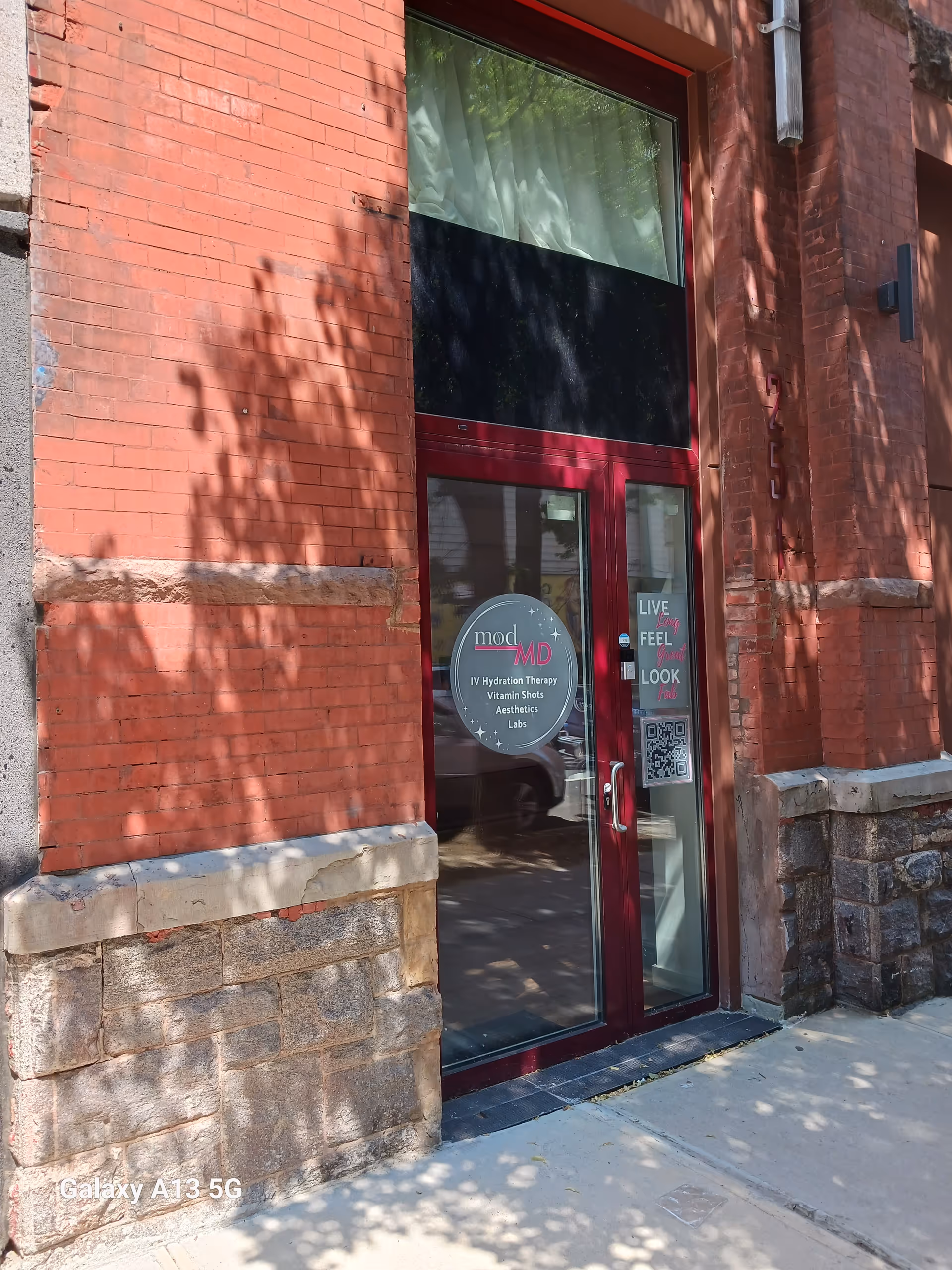 Red brick building entrance with glass door and circular ModMD sign; shadows on sidewalk.