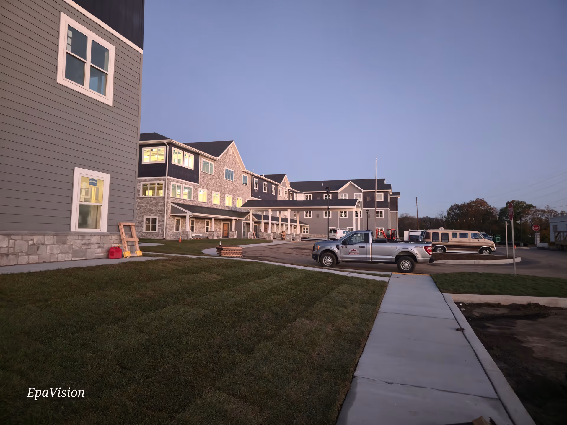 Exterior view of a senior living facility with parked vehicles along a sidewalk.