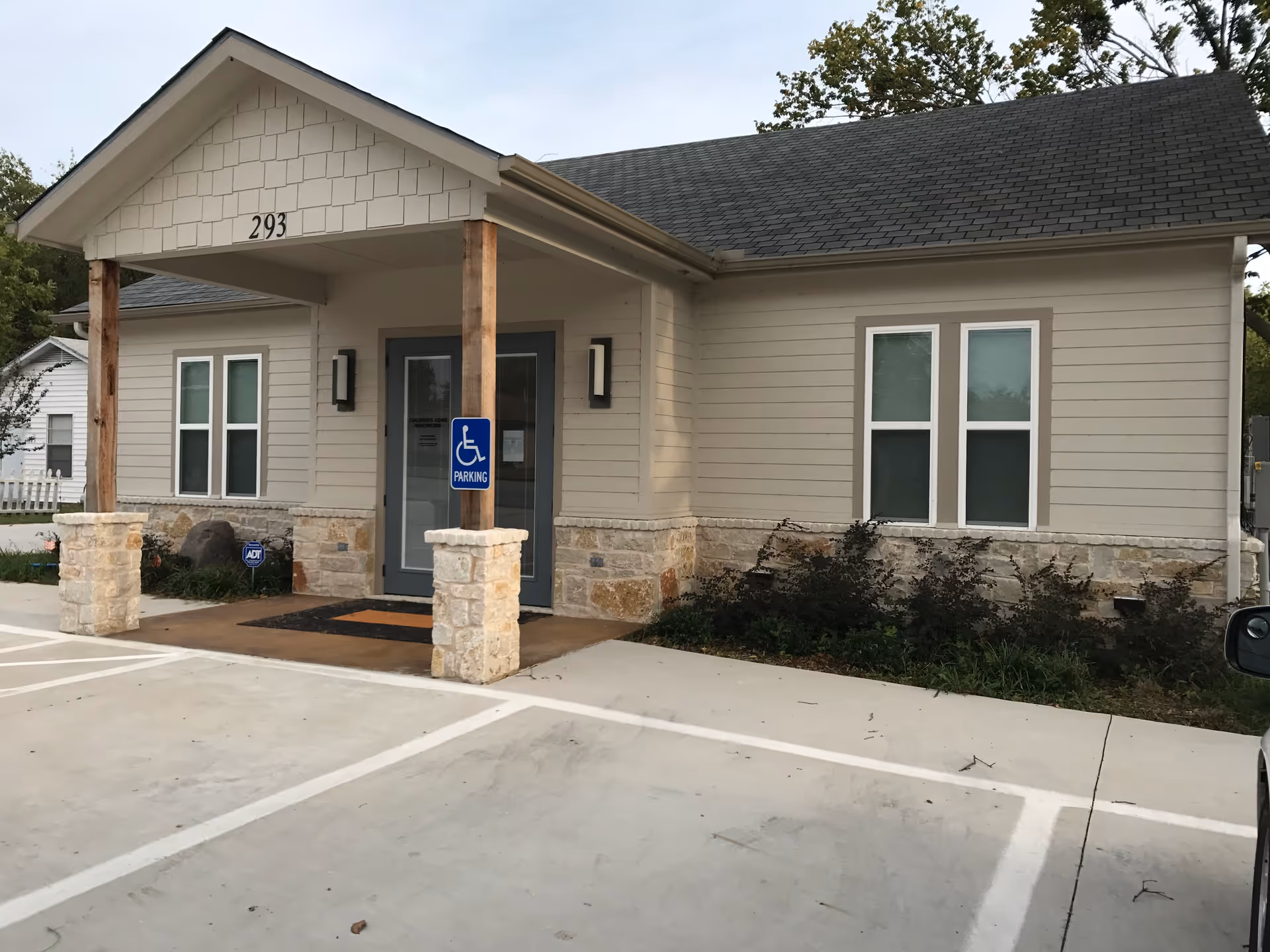 Single-story beige building with stone base and covered entrance, handicapped parking in front
