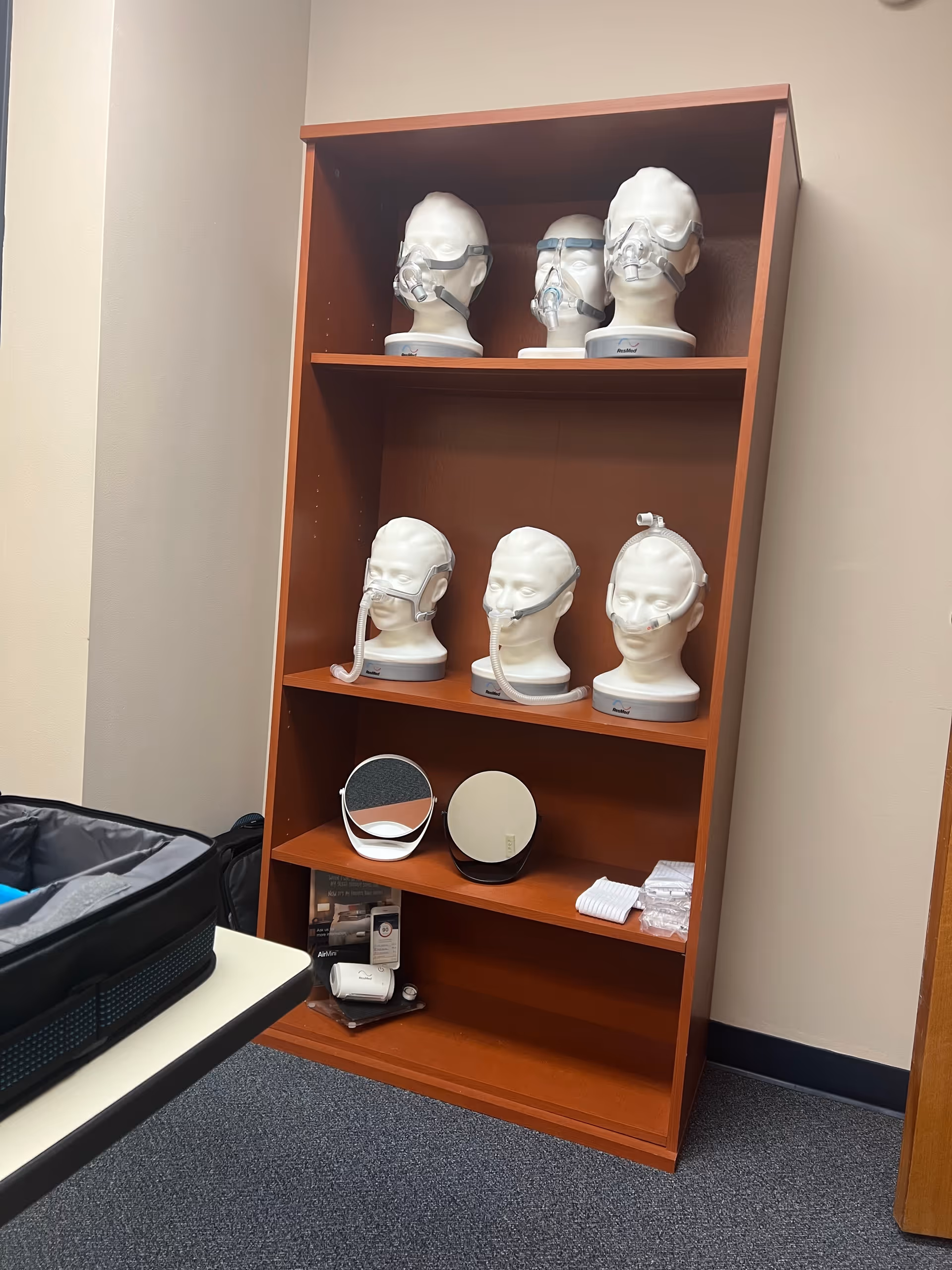 Wooden shelf with CPAP masks on mannequin heads and accessories in a clinical interior.