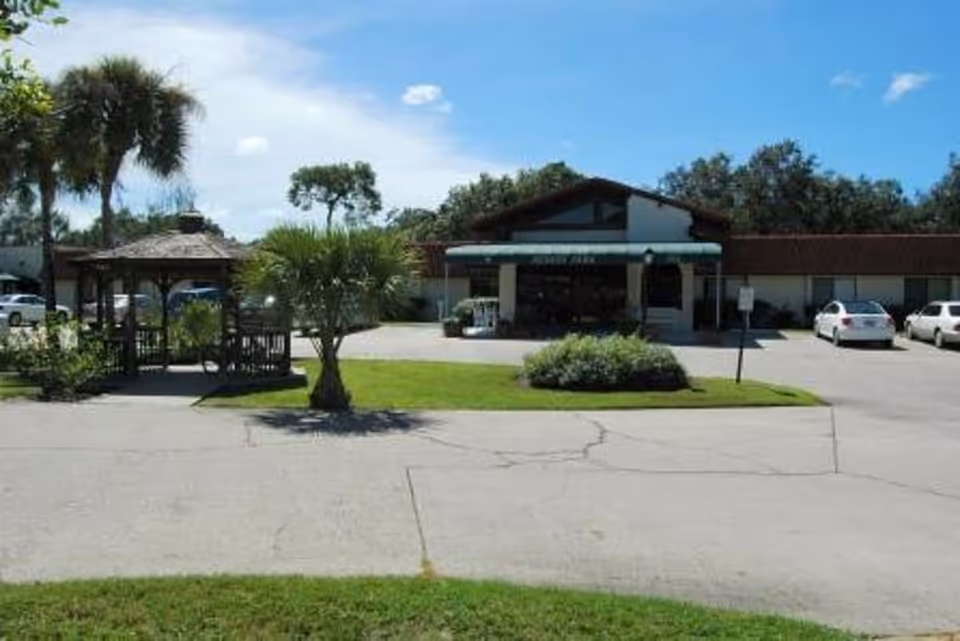 Front exterior of a single-story building with a covered entrance, gazebo, palm trees, and a parking lot.