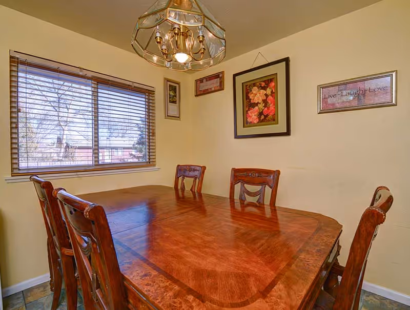 A dining room with a wooden table and chairs, wall art, and a window.