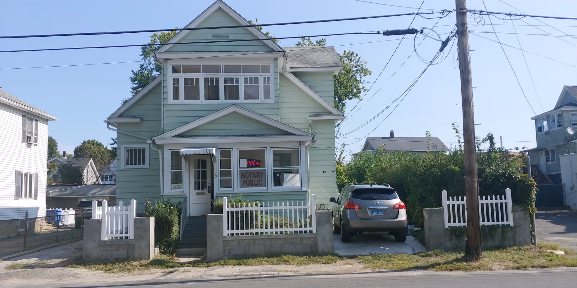 Green two-story house with white railings, a car, and a notary public sign.