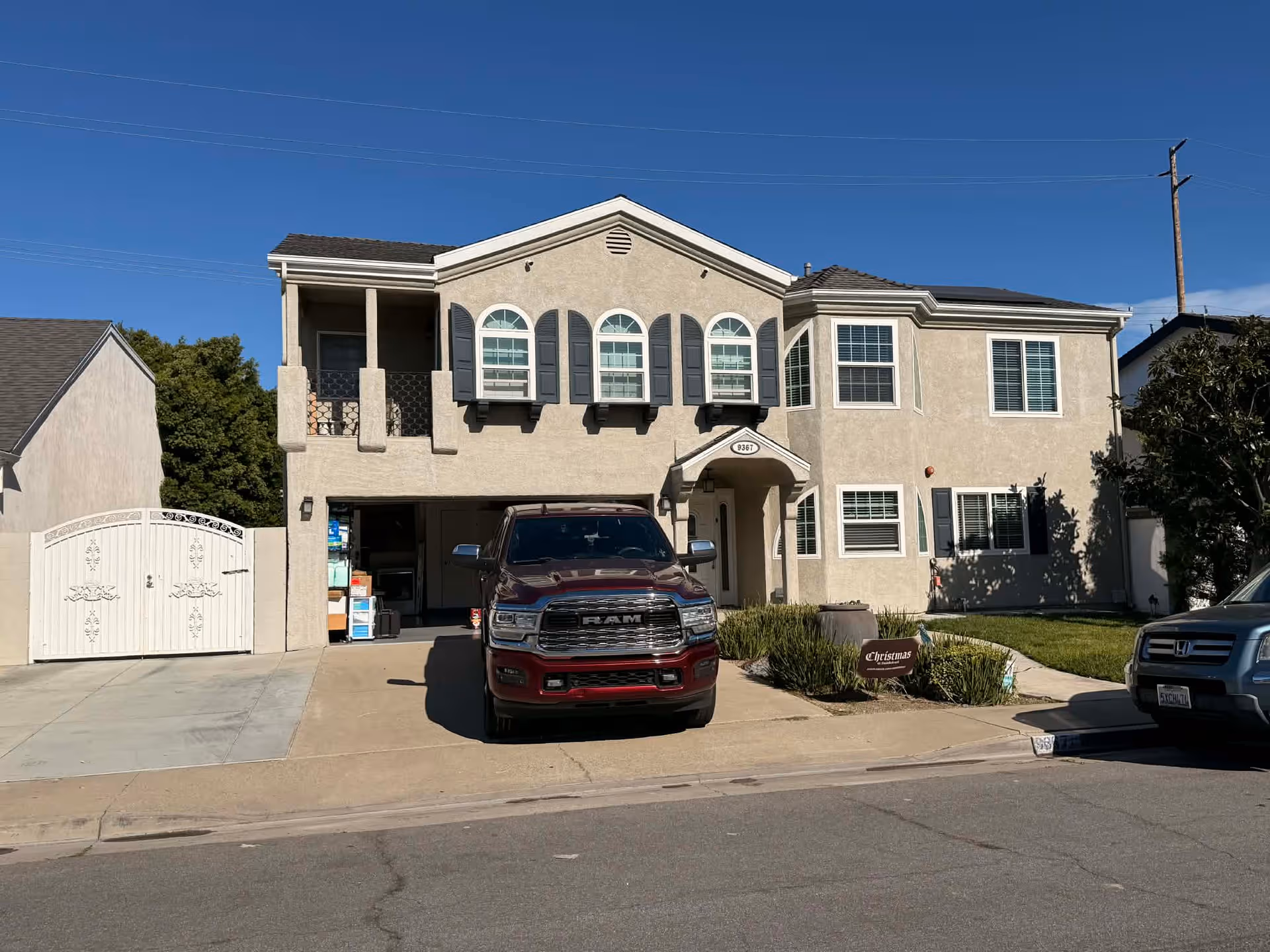 Two-story beige senior-living building with a driveway, parked trucks, and a gated entrance.