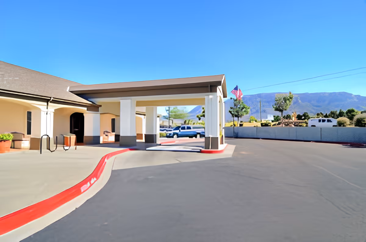 Covered porte-cochere entrance and driveway of a senior living building with potted plants and mountains in the background.