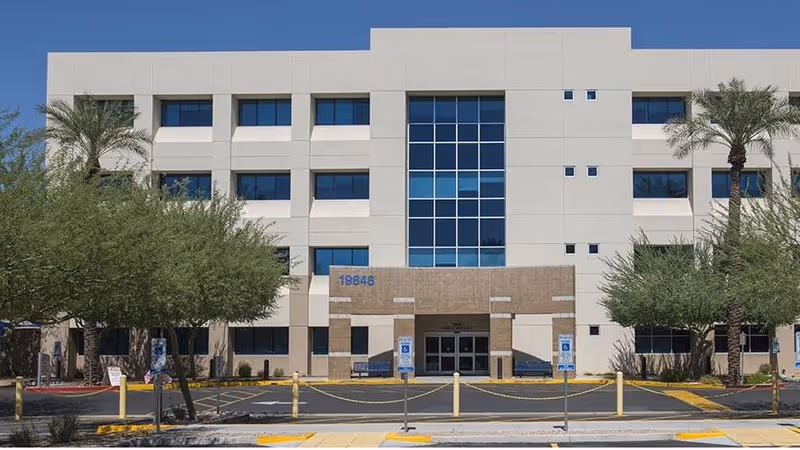 Modern medical center exterior with glass facade, palm trees, and main entrance.