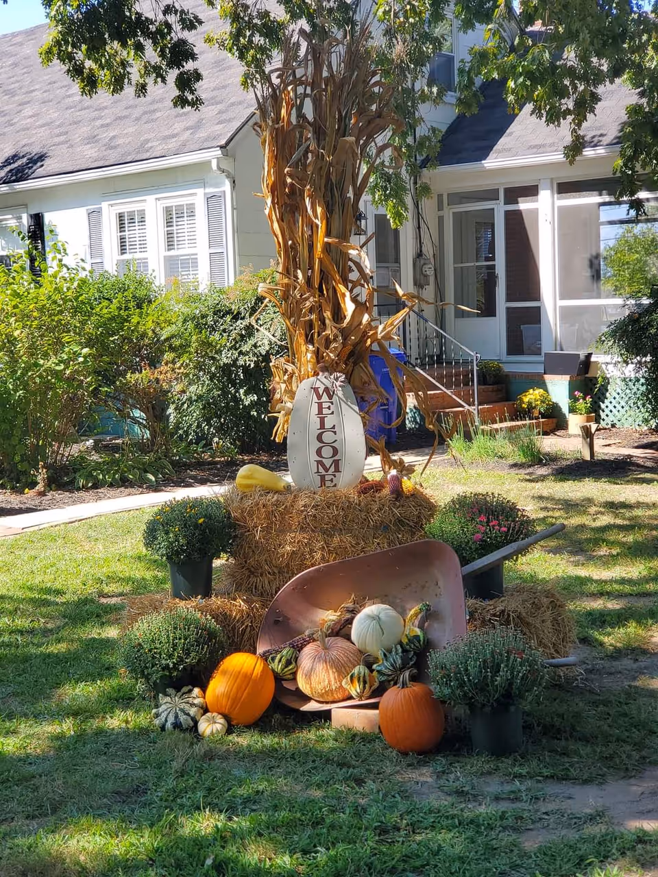 Front lawn decor with pumpkins, hay bales, and autumn arrangements in front of a residence.