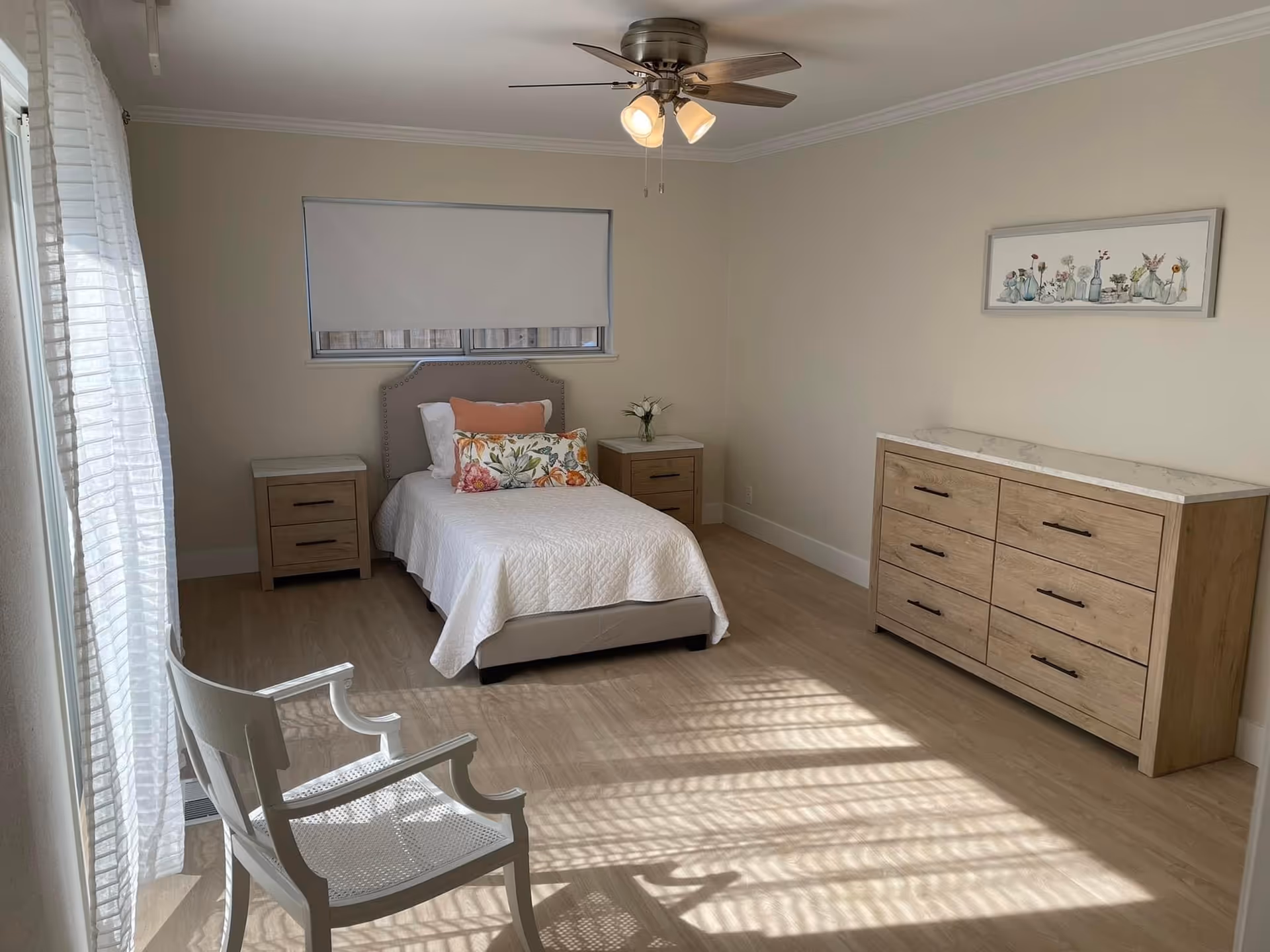 Bright, neatly furnished bedroom with bed, dressers, nightstands in a senior living facility.