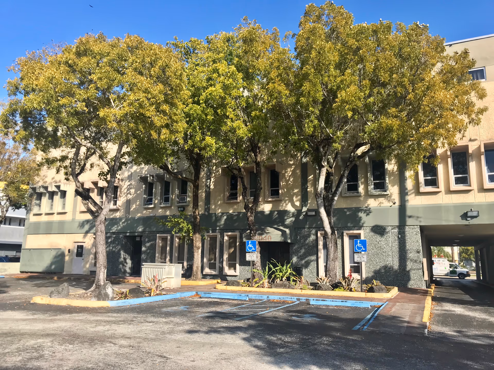 Front exterior of a two-story beige building with green accents and trees