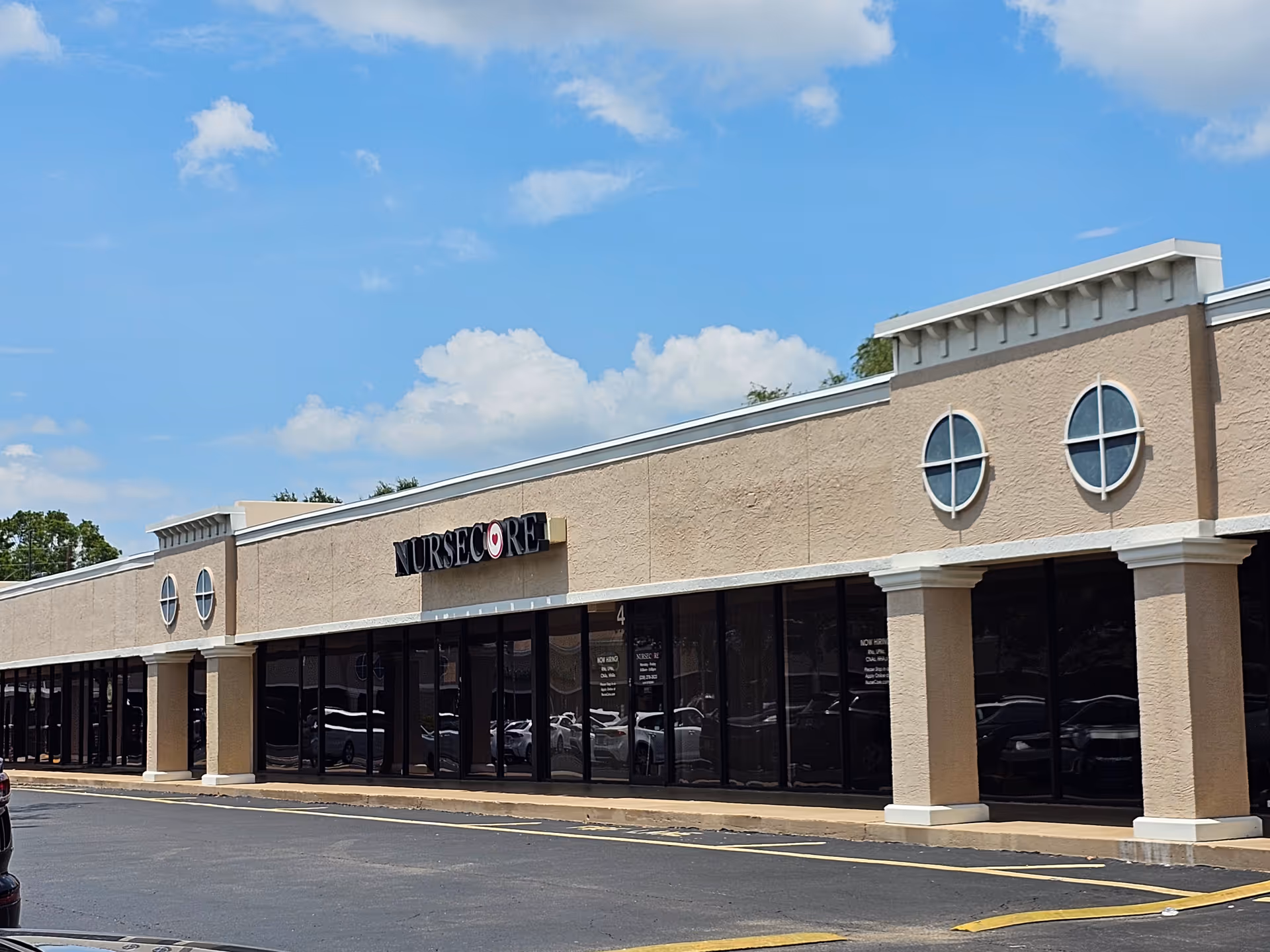 Exterior view of a beige building with large glass storefront and round windows under blue sky.