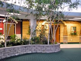 Exterior view of Guardian Angels Health and Rehab Center with yellow wooden cottages and landscaping.