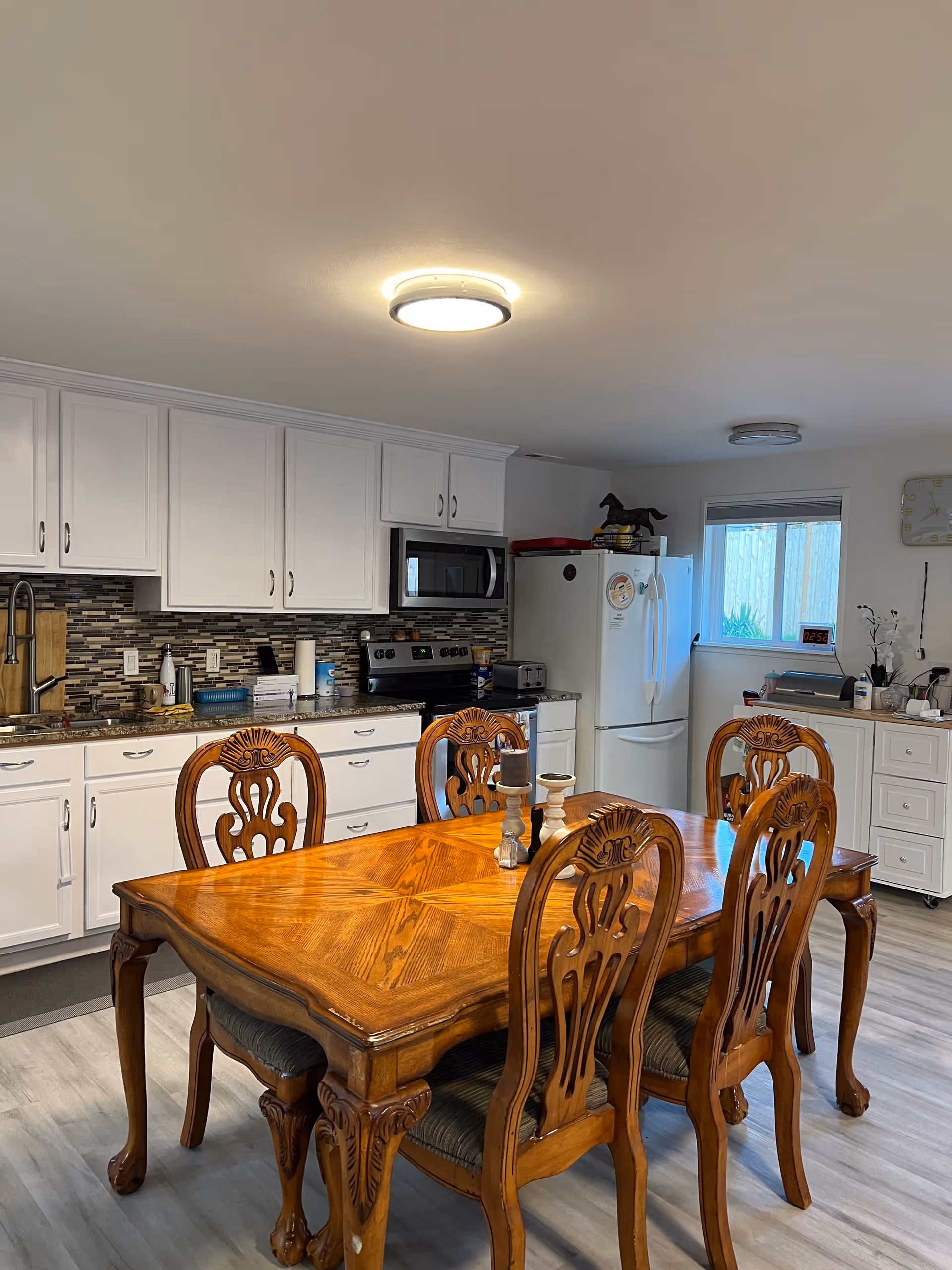 Bright kitchen-dining area with white cabinets, a large wooden dining table and chairs.