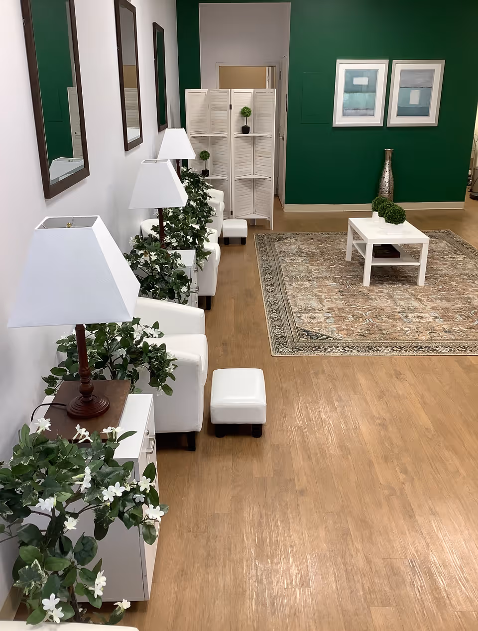 White seating area with lamps, plants, and a rug in a green-walled lounge.