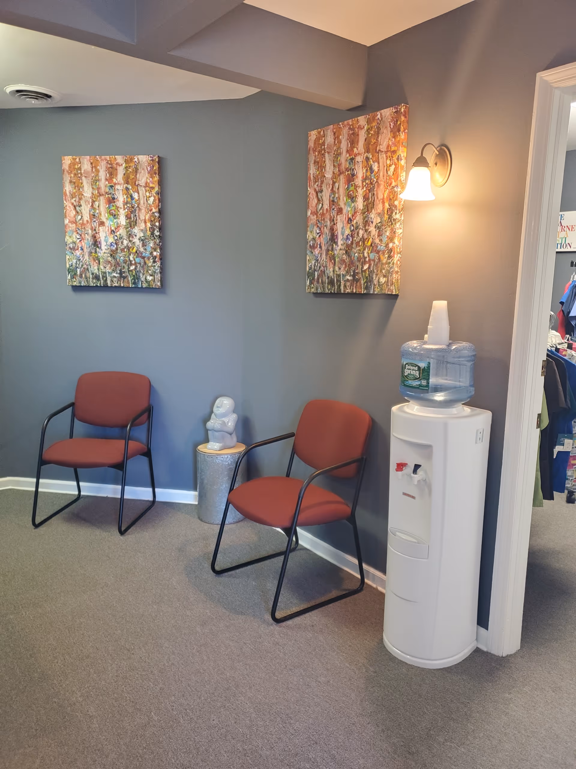 Interior waiting area with two red chairs, a water cooler, and abstract paintings.