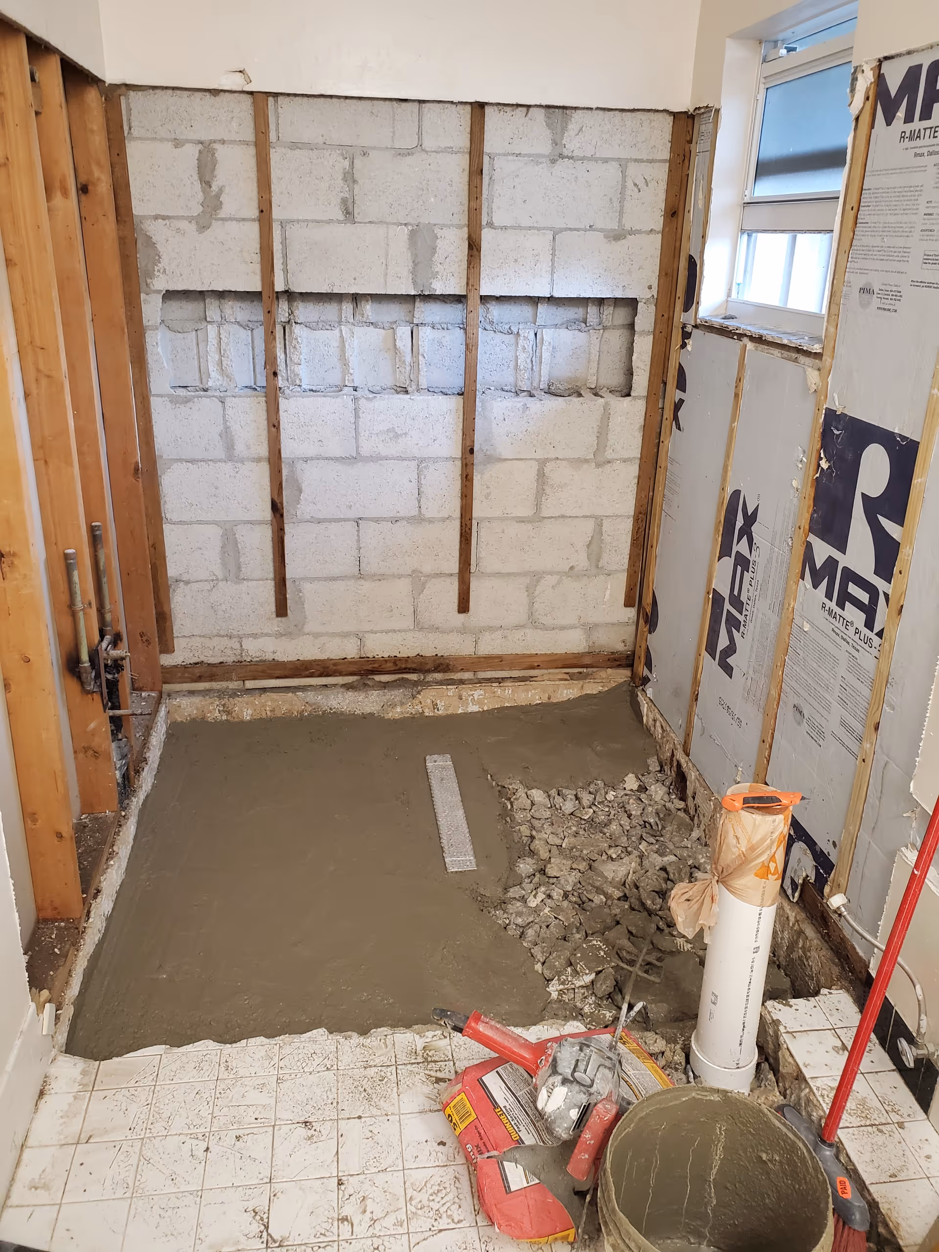 Bathroom under renovation with exposed studs, concrete blocks, plumbing, and construction debris.