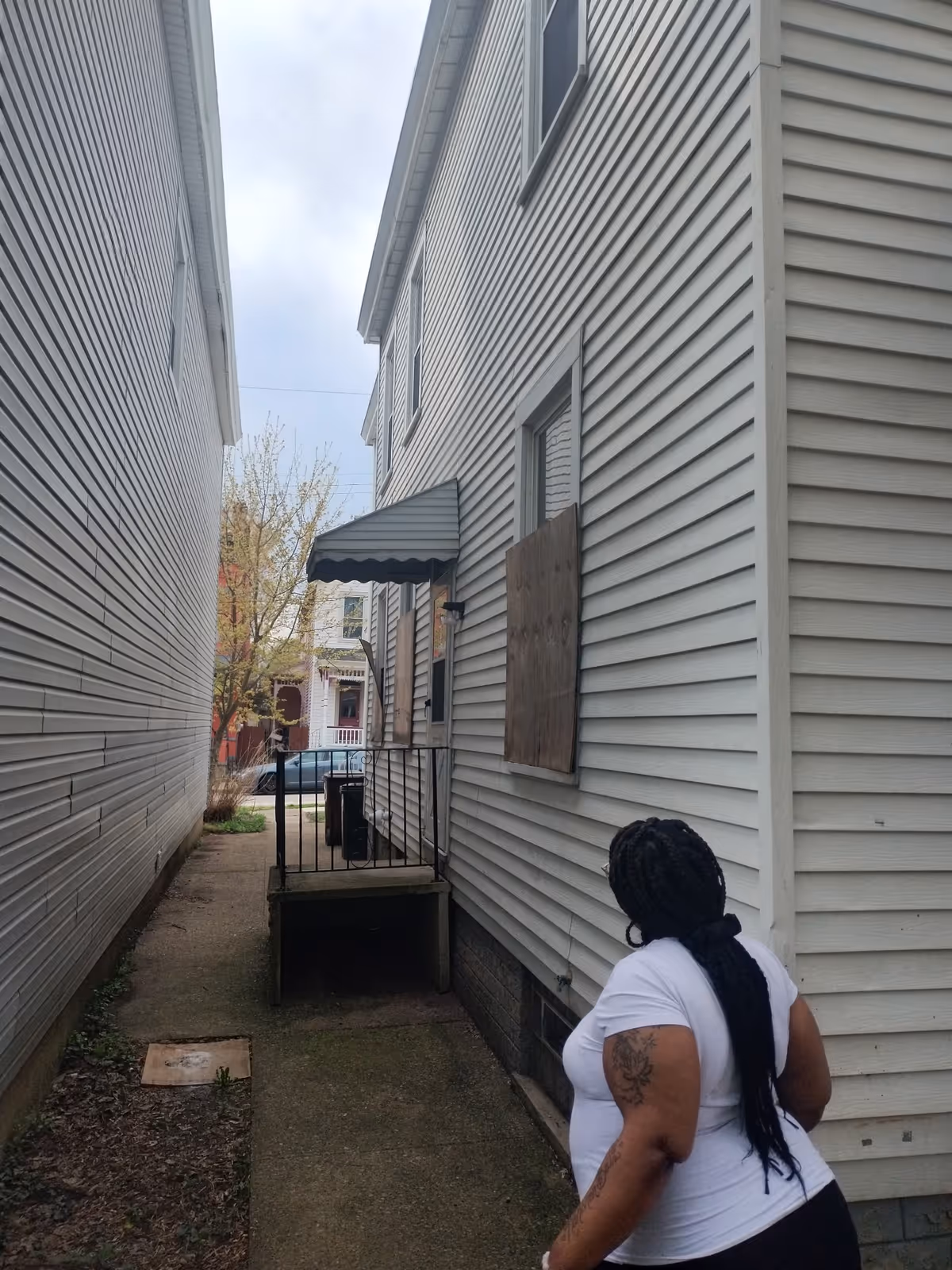 Person in white shirt walks along narrow exterior walkway between beige siding buildings.
