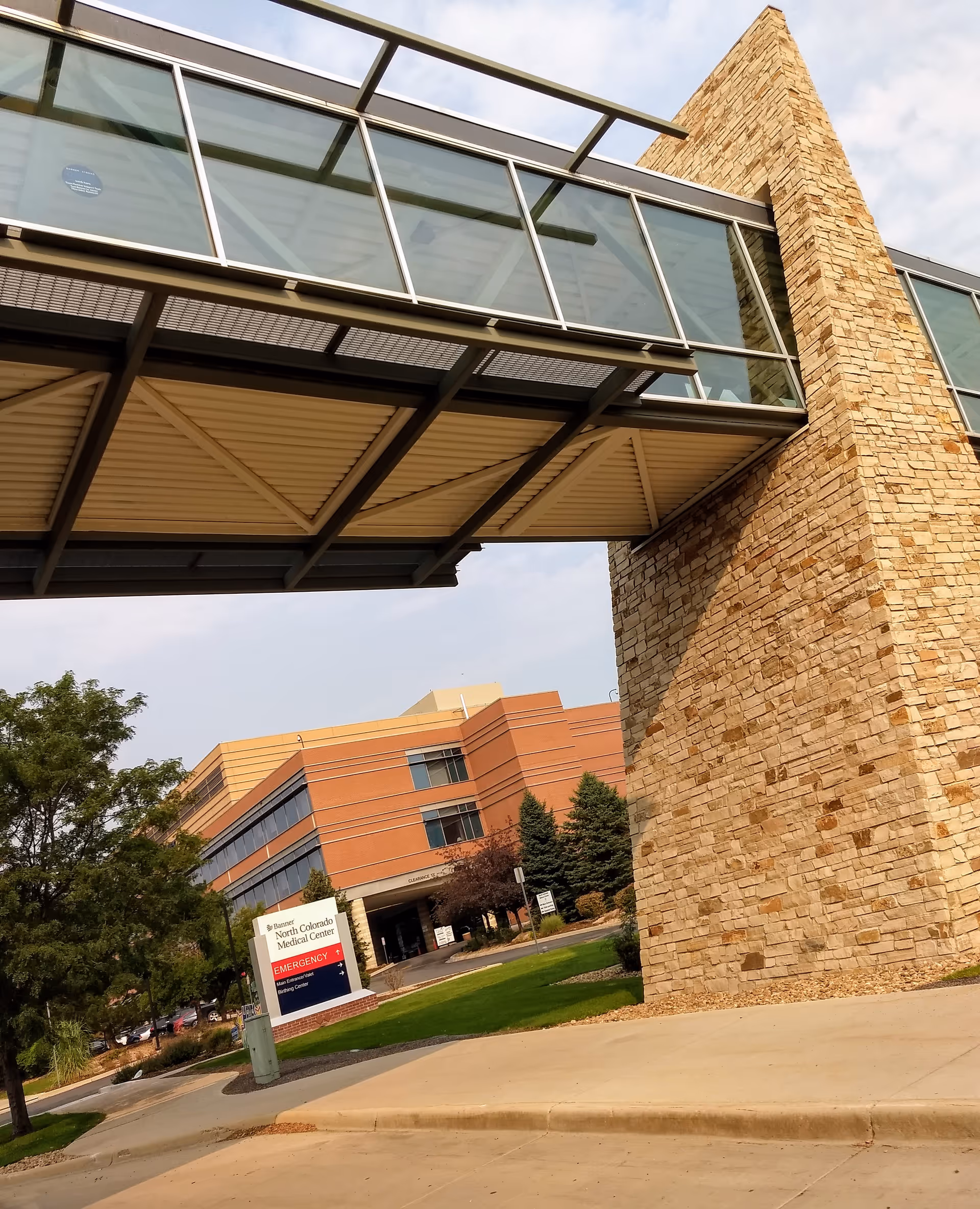 Glass-enclosed walkway spans a stone pillar to the Banner North Colorado Medical Center exterior.