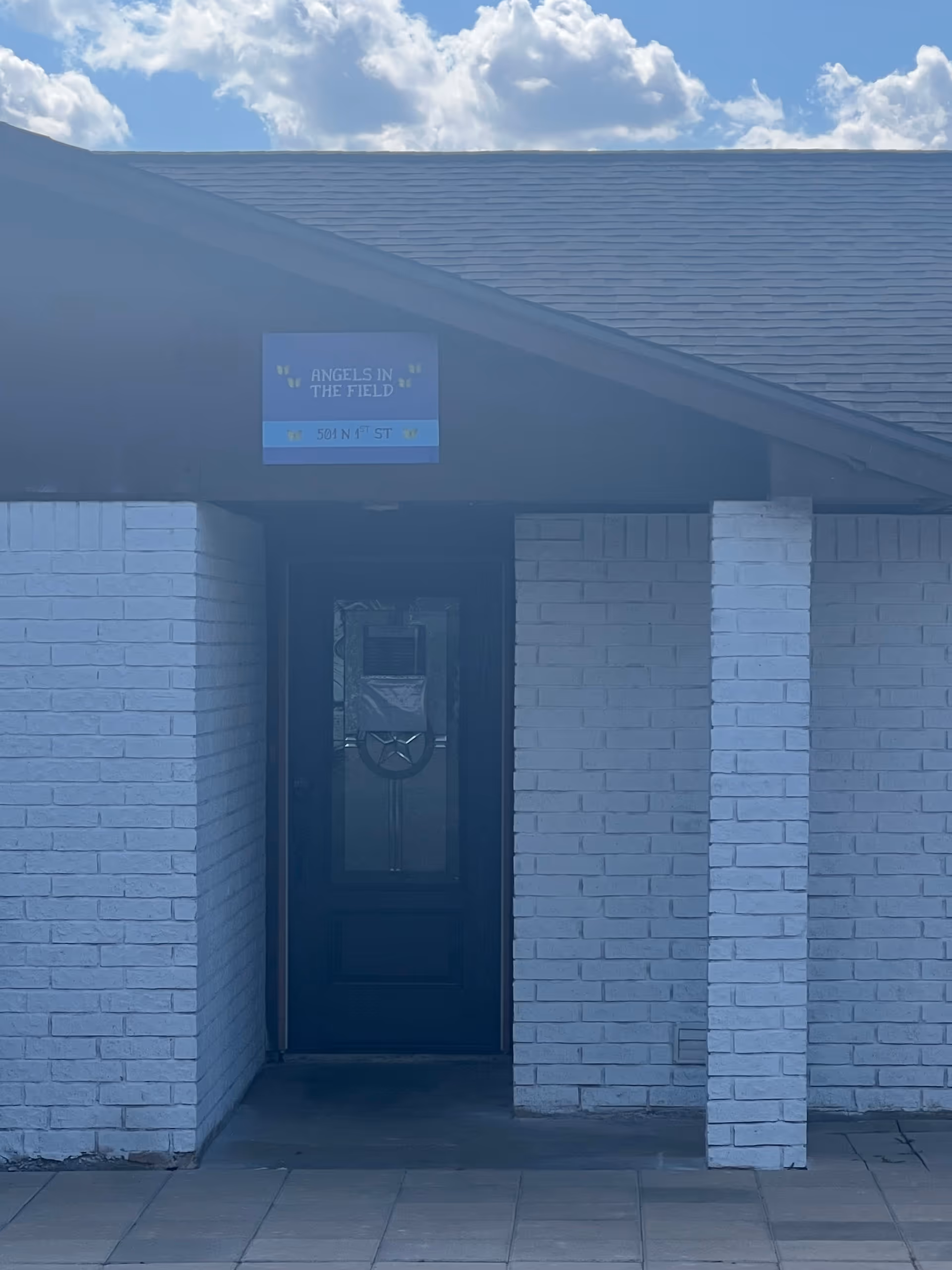 Exterior entrance to Angels in the Field facility with a blue sign above the door.