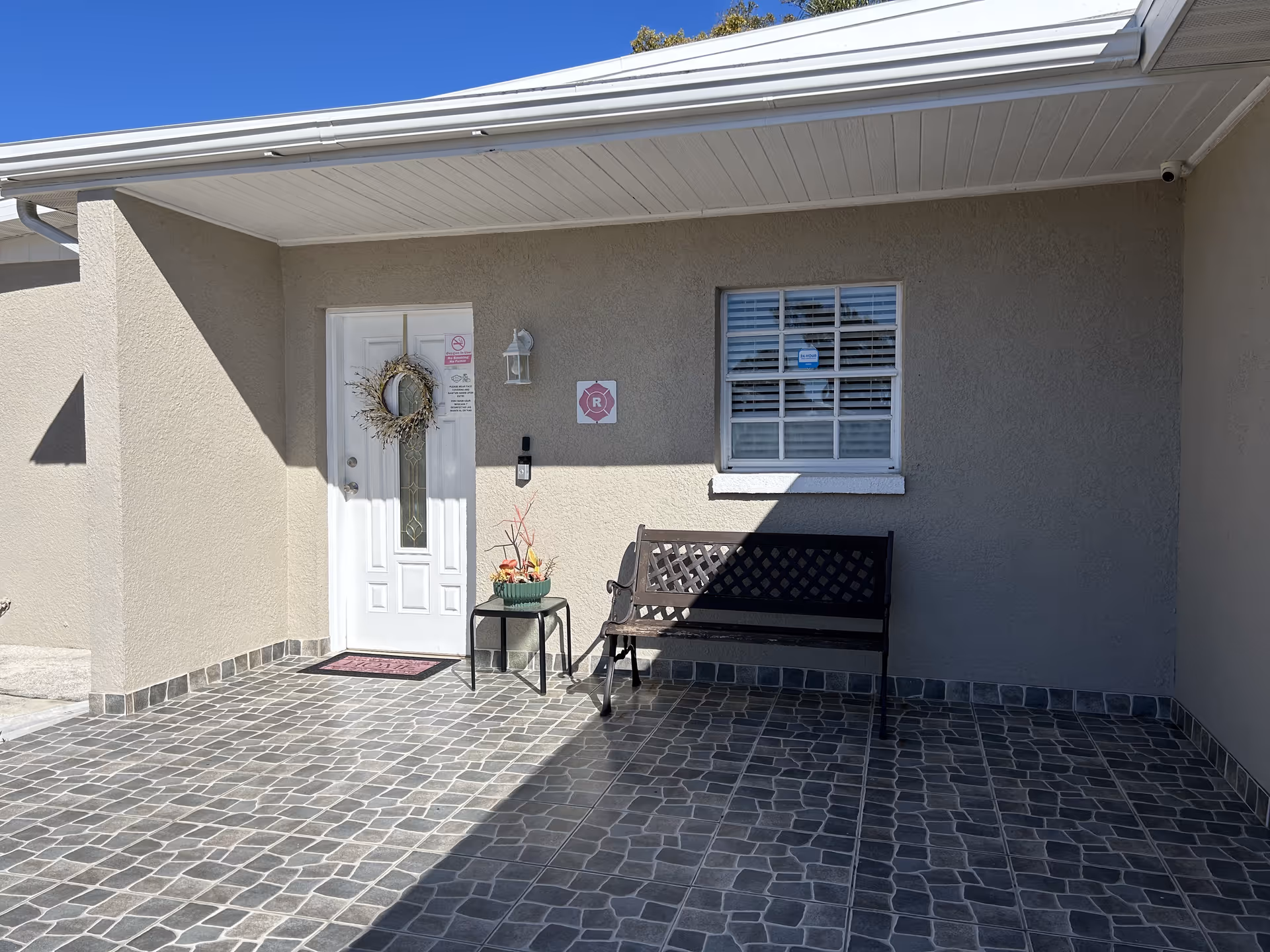 Exterior entrance with a door, wreath, window, and bench on a tiled front porch.