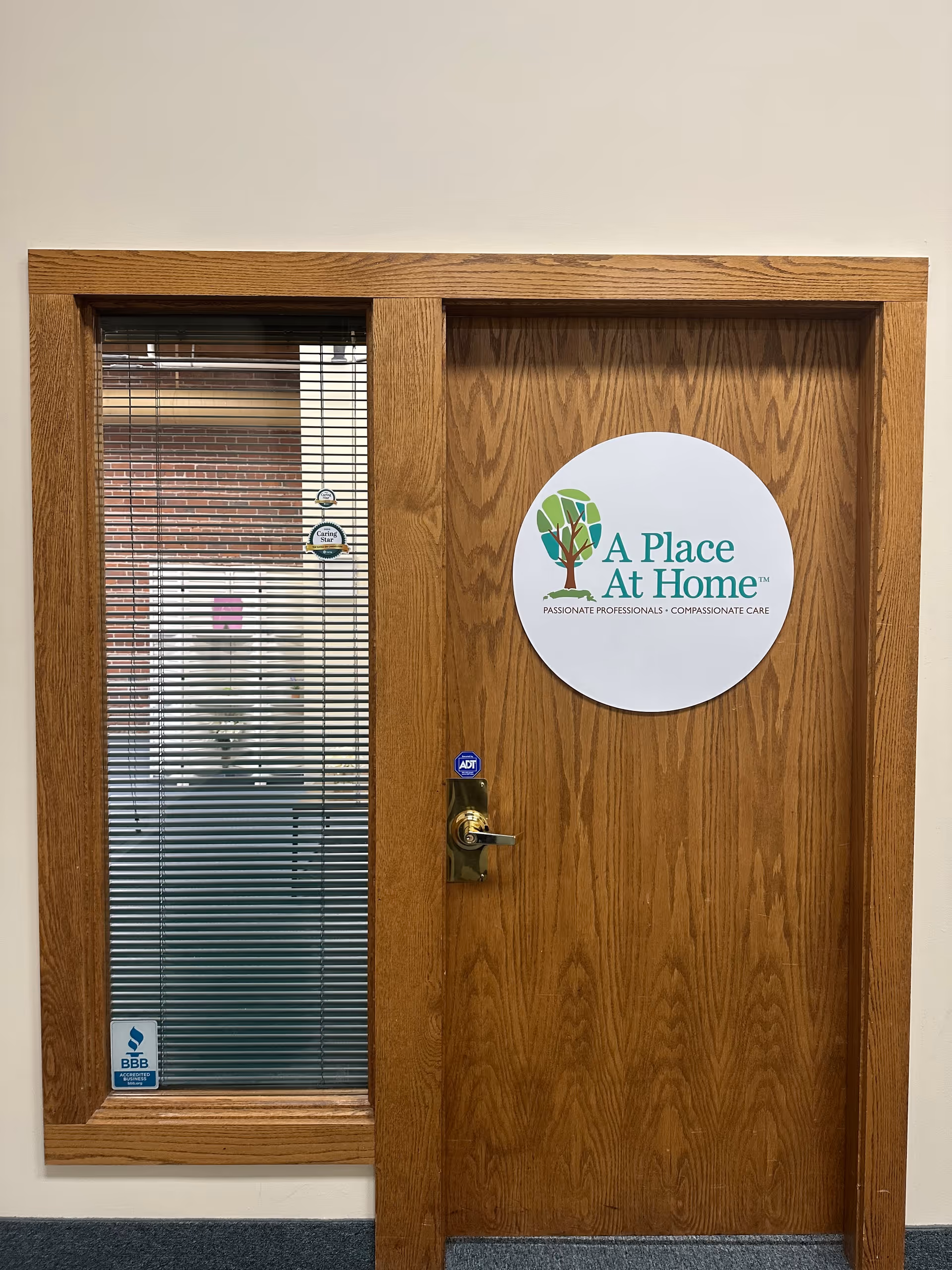 Wooden door with circular A Place At Home sign beside a glass window panel