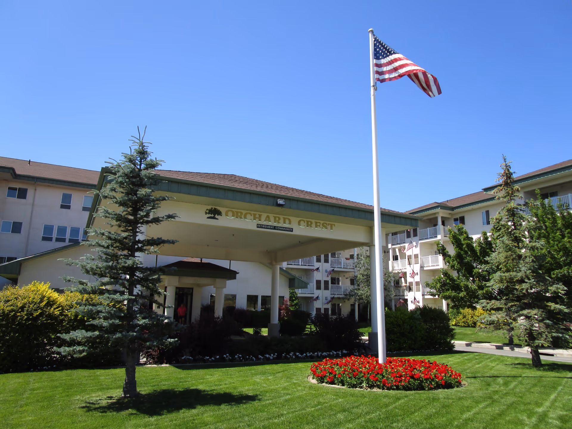 Orchard Crest retirement community entrance with flagpole, manicured lawn, and surrounding landscaping.