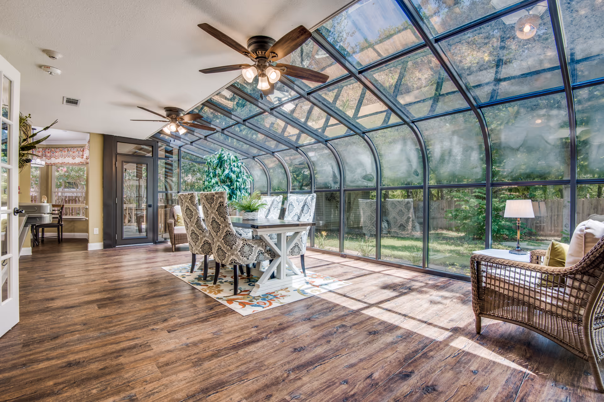 Sunlit indoor sunroom with glass ceiling, wood floors, and a central dining area.