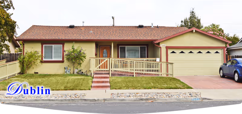 Front view of a single-story beige house with a ramp, lawn, and attached two-car garage.