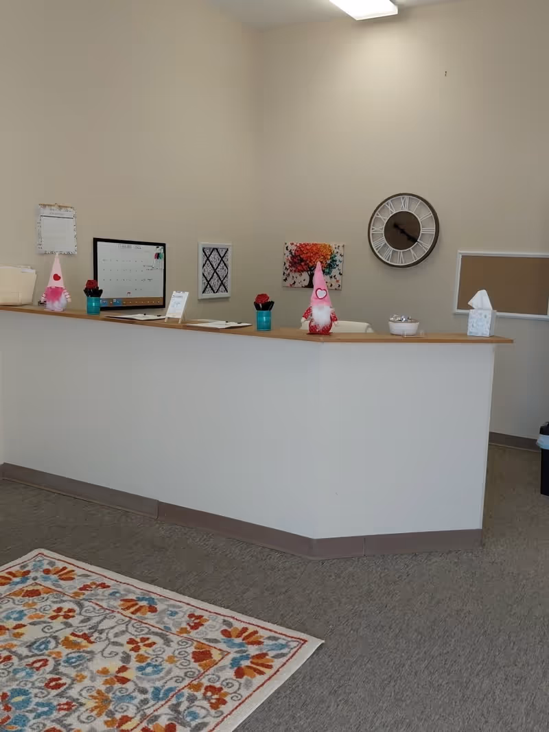 Reception area with a long counter, clock, wall art, and a colorful rug.