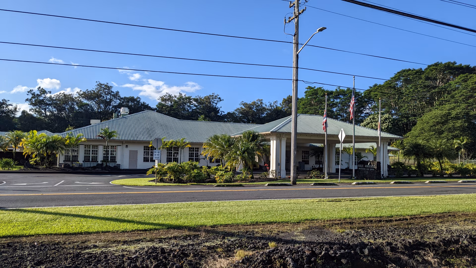 Front view of Hale Anuenue Restorative Care, a single-story building with flags and palms.