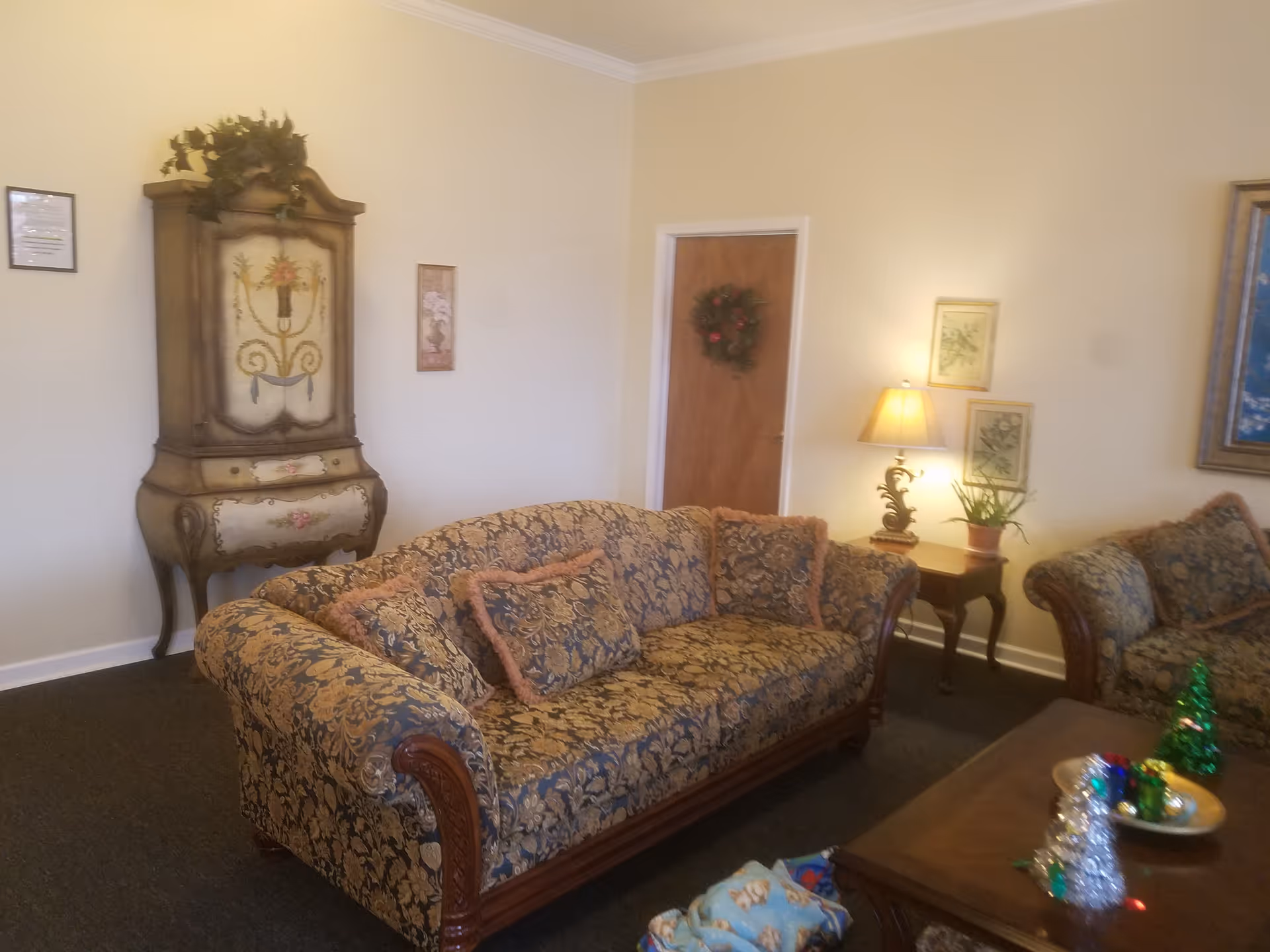 Traditional living room with a patterned sofa, antique cabinet, lamps, and festive decorations.