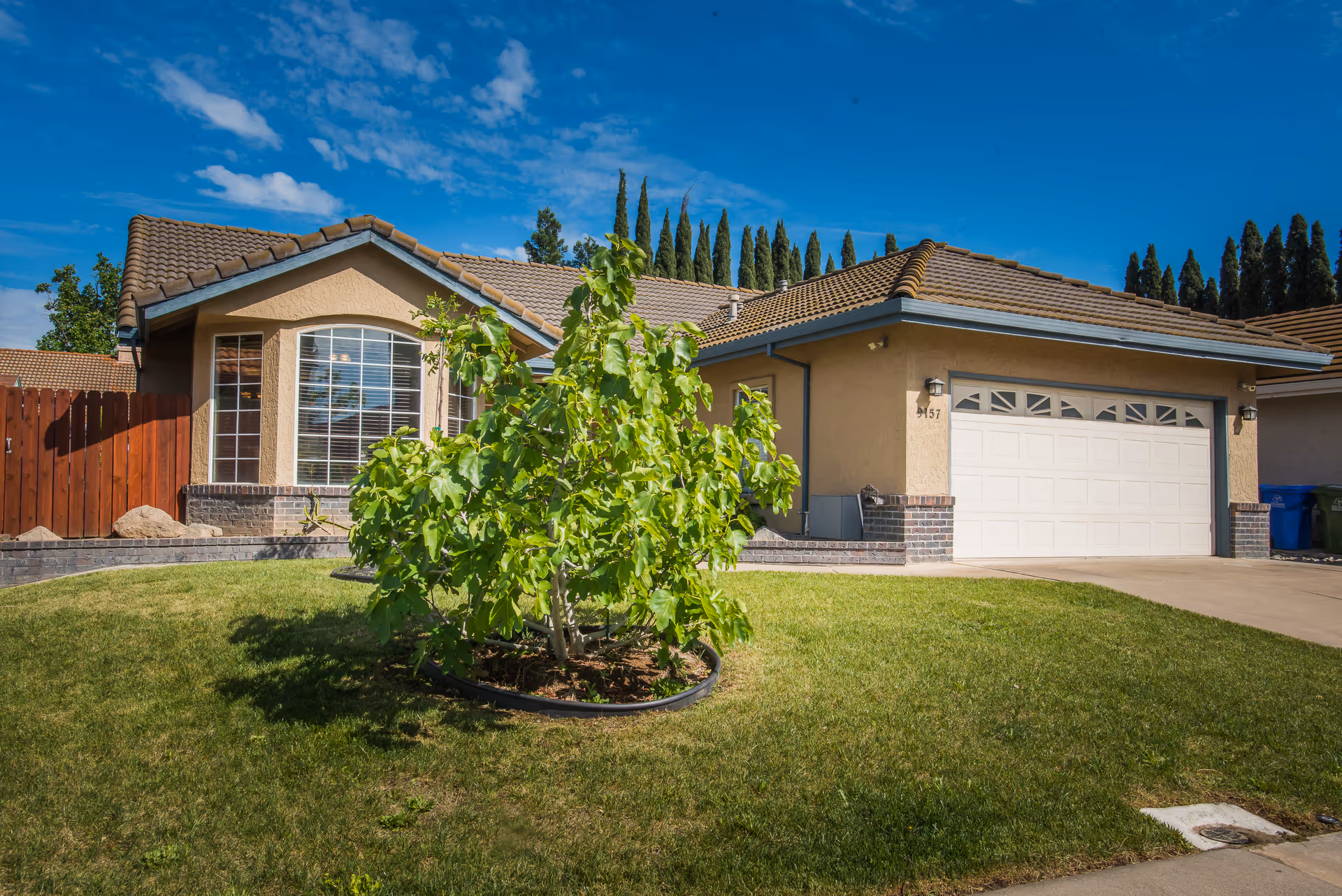 Front view of a beige, single-story house with attached two-car garage and manicured lawn